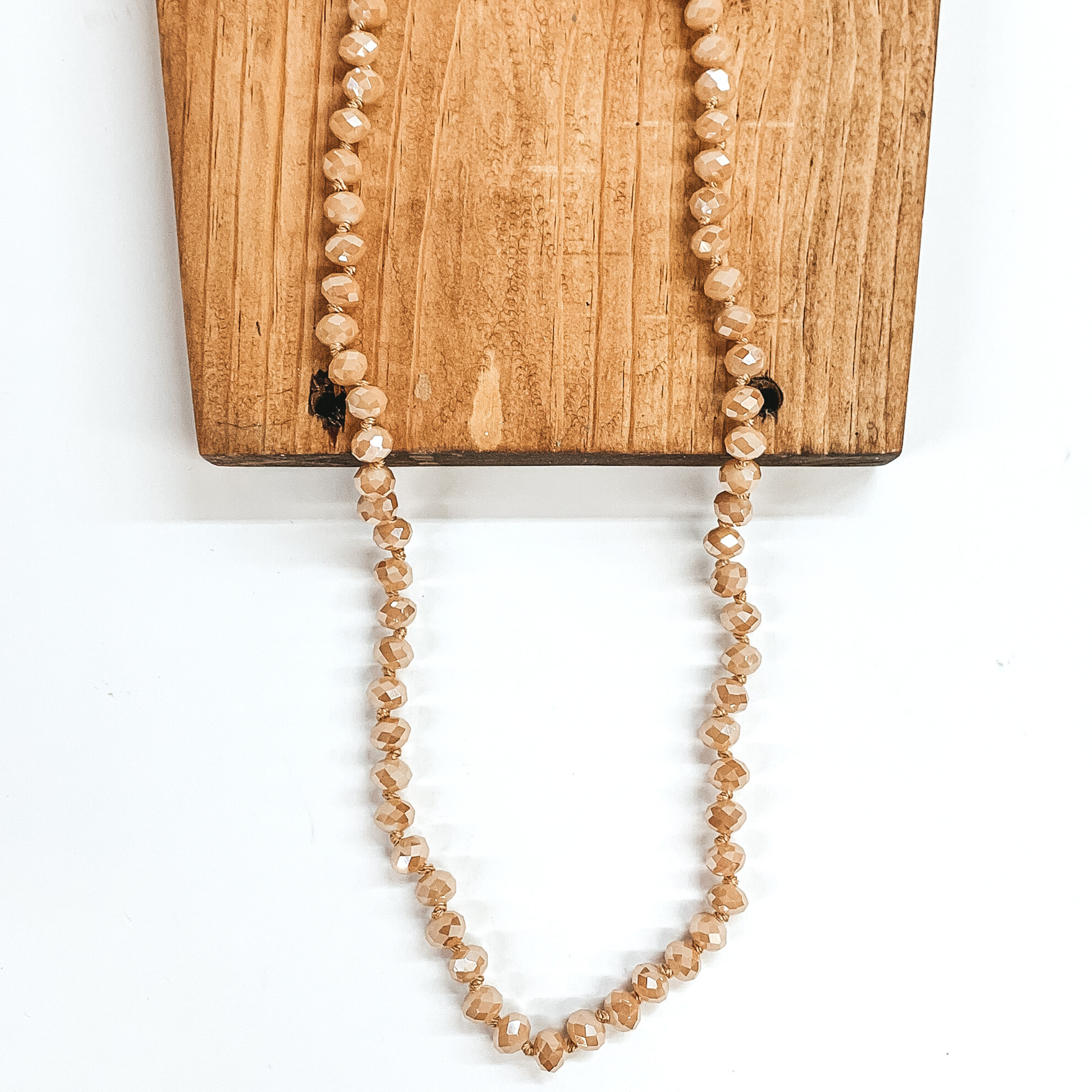Sand colored crystal beaded necklace. This necklace is pictured on a brown block on a white background.