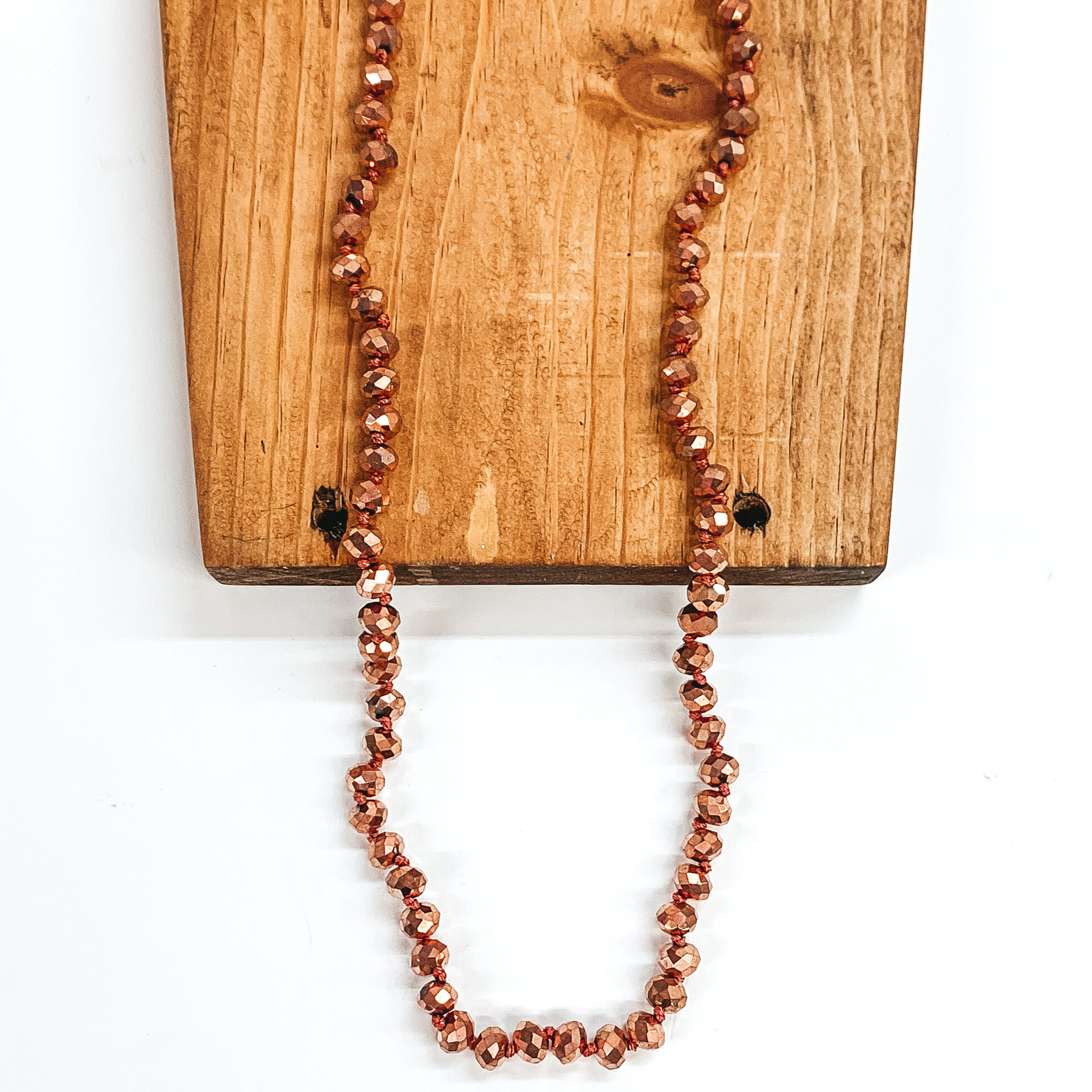 Rose gold crystal beaded necklace. This necklace is pictured on a brown block on a white background.