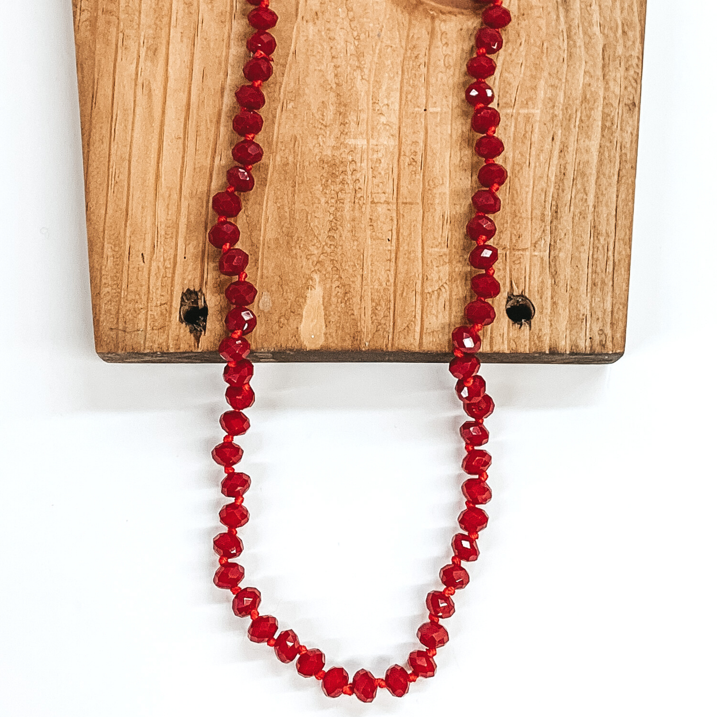 Dark red crystal beaded necklace. This necklace is pictured partially laying on a brown block on a white background. 