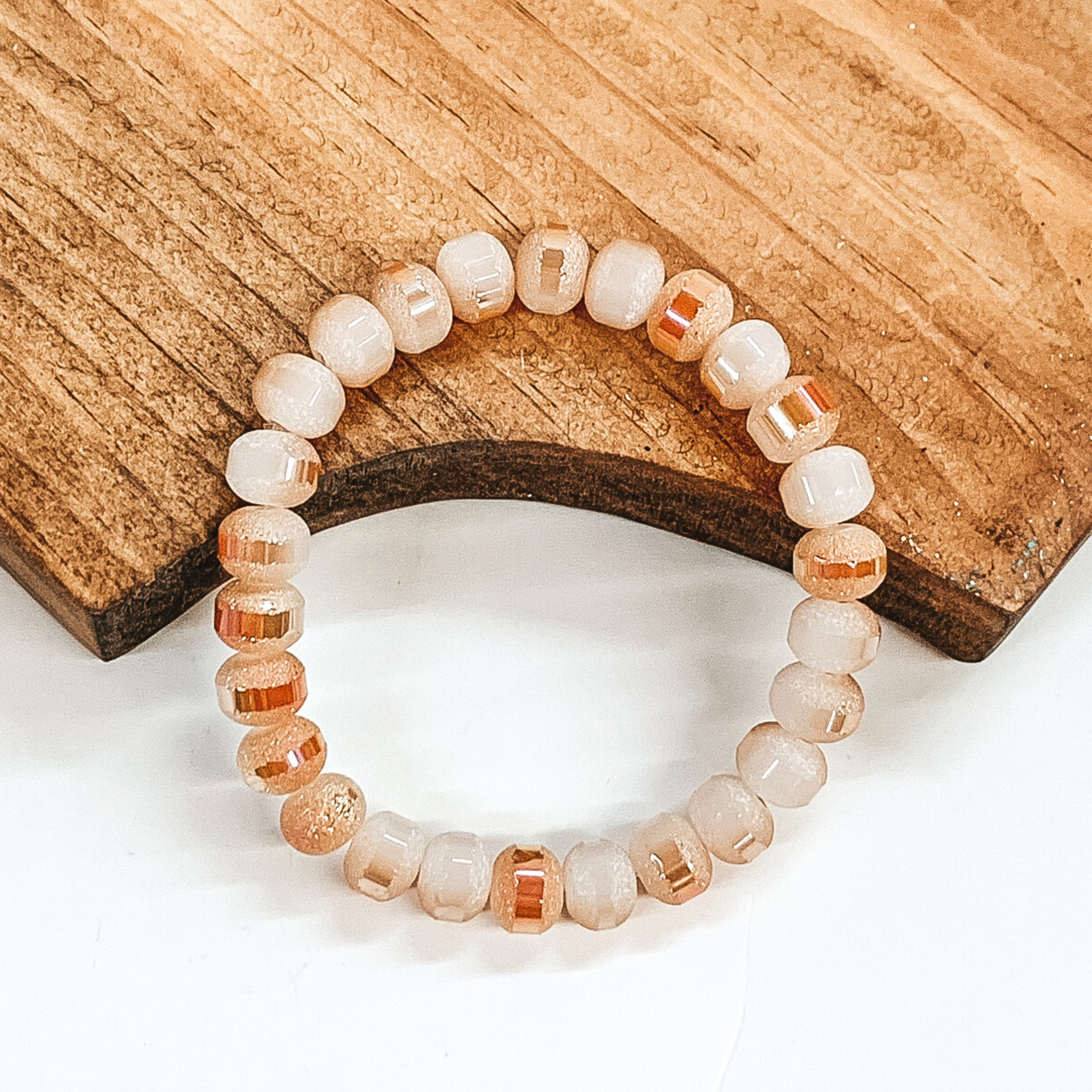 Crystal beaded bracelet in light pink and tan. This bracelet is pictured on a partially laying on a brown block on a white background.