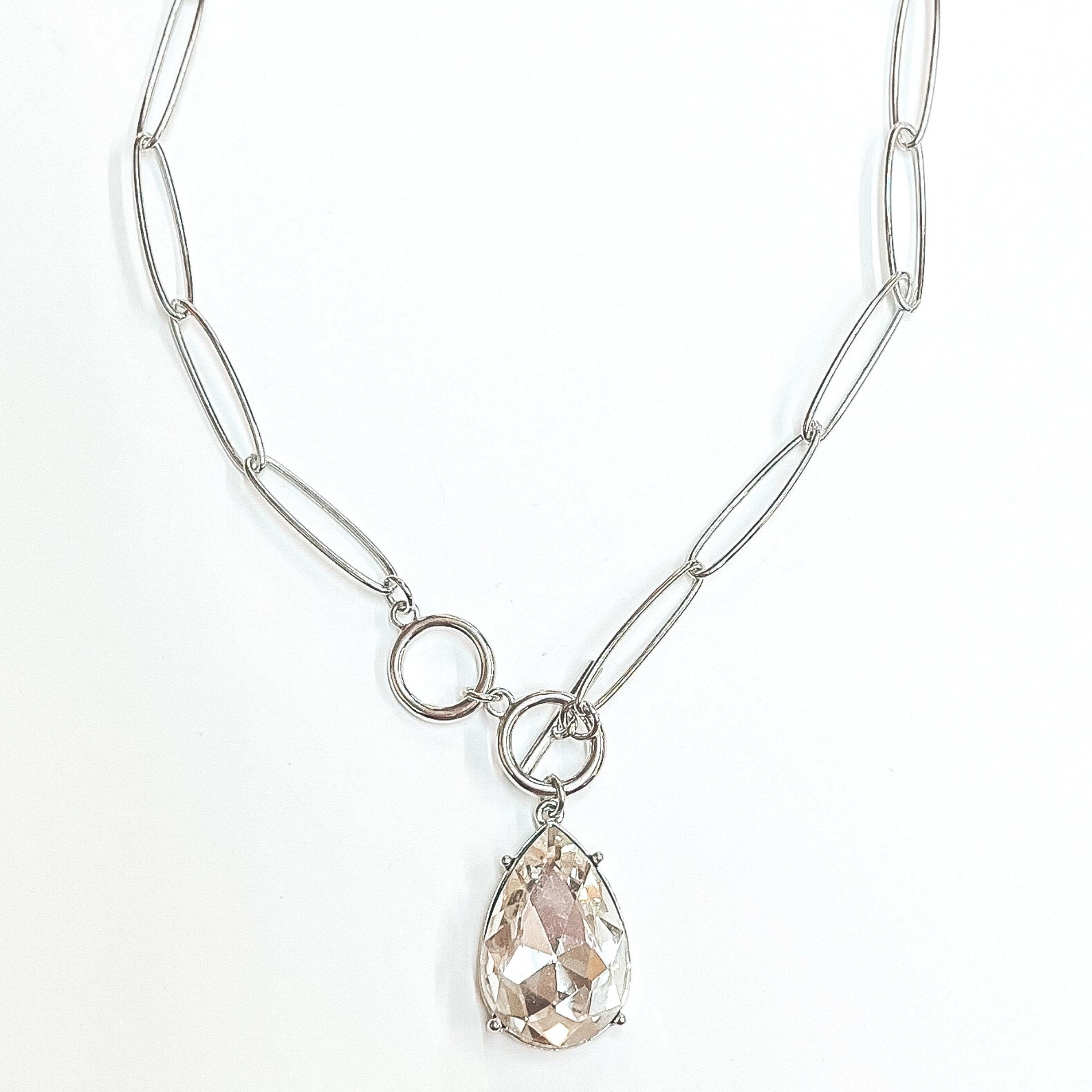 Silver, thin chain necklace with front toggle clasp. This necklace includes a clear teardrop crystal. This necklace is pictured on a white background. 