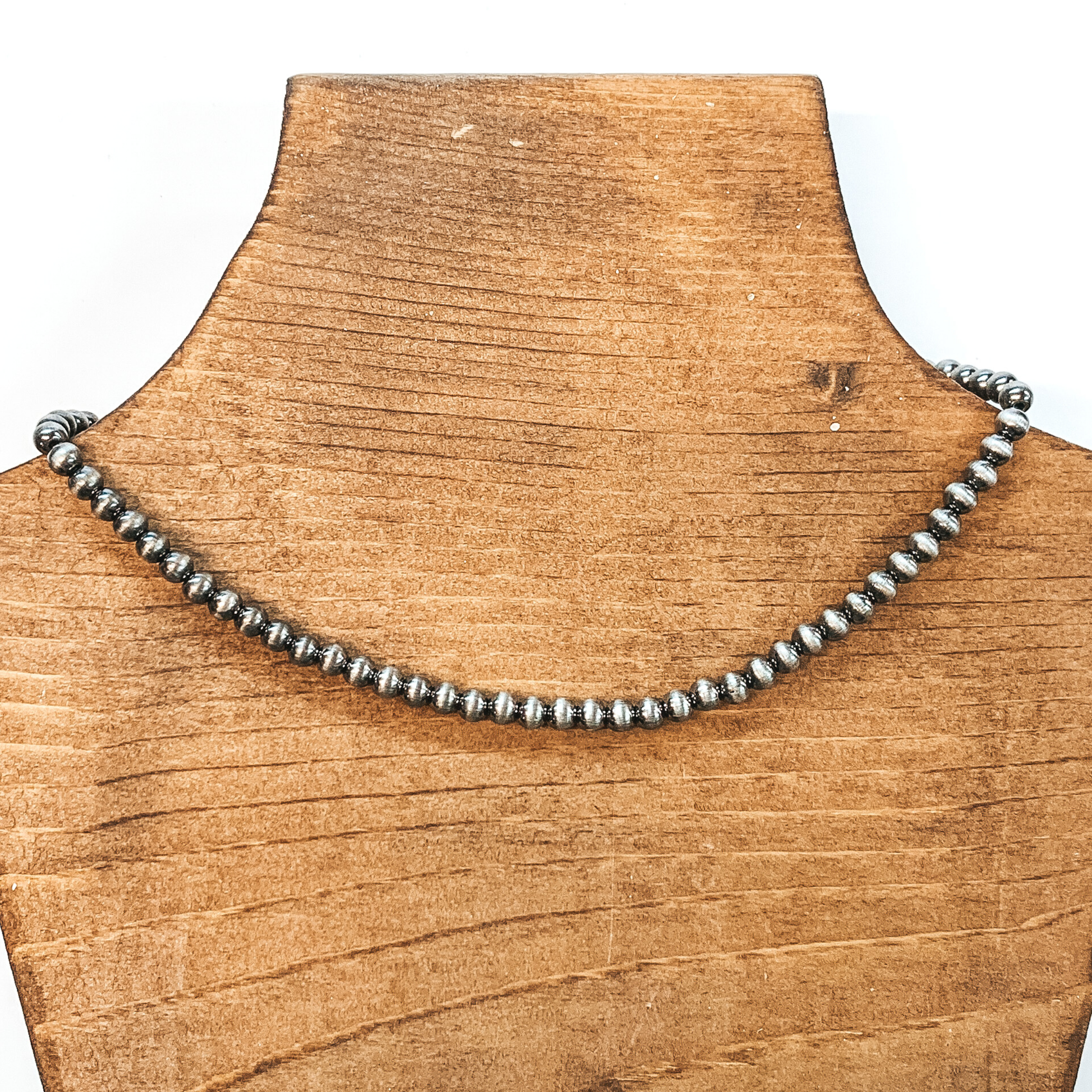 Silver beaded necklace. This necklace is pictured on a brown necklace holder on a white background.