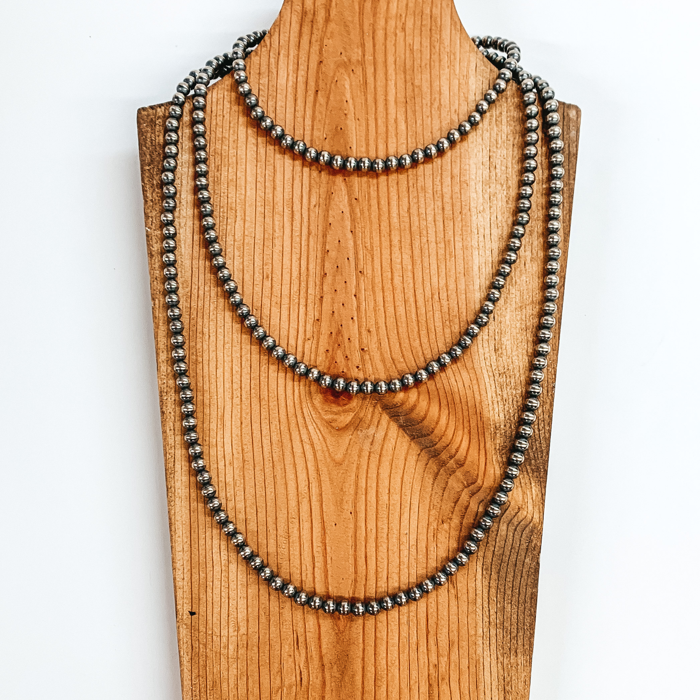 Layered silver beaded necklace pictured on a brown necklace holder on a white background. 