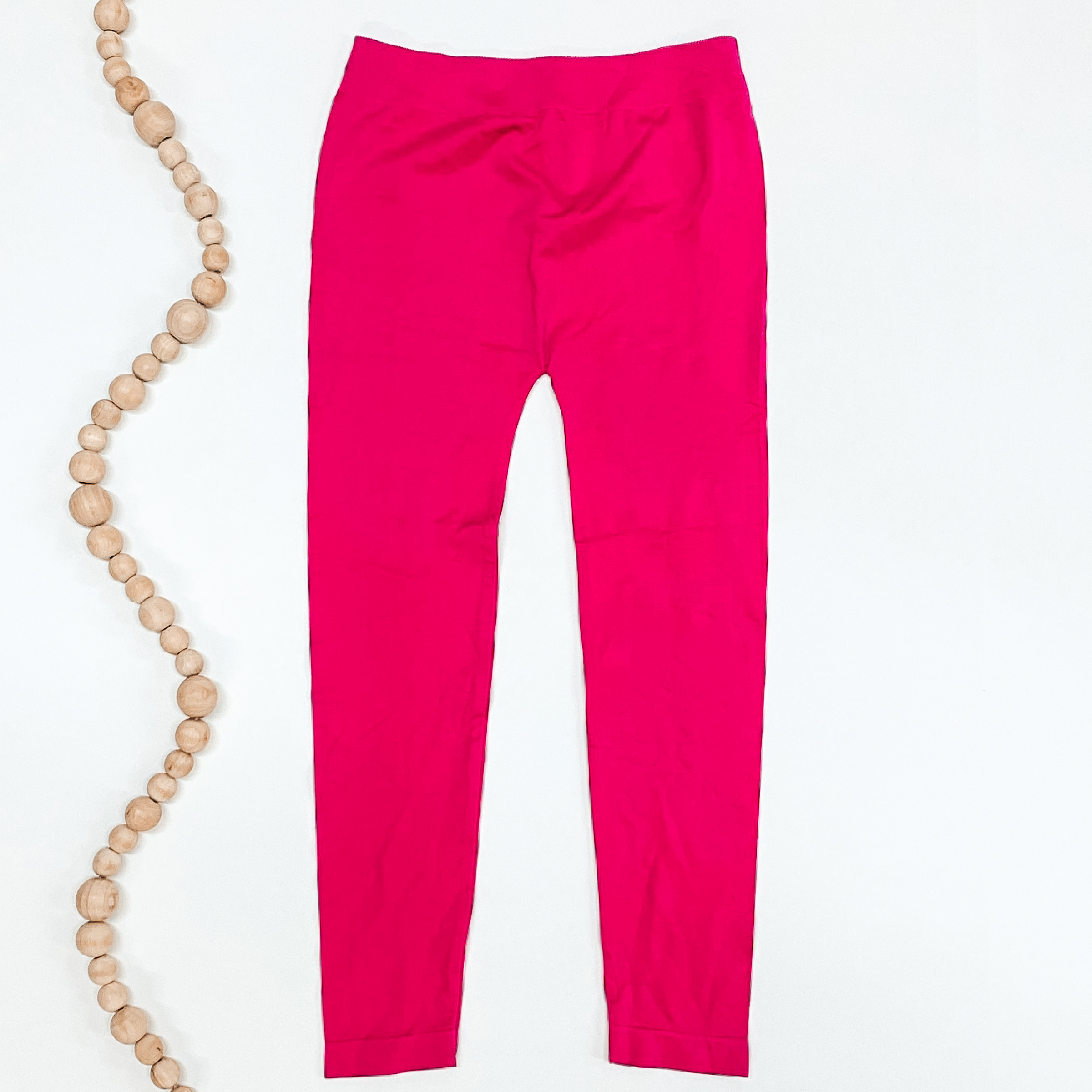 Hot pink colored leggings pictured on a white background with tan beads to the left of the leggings.