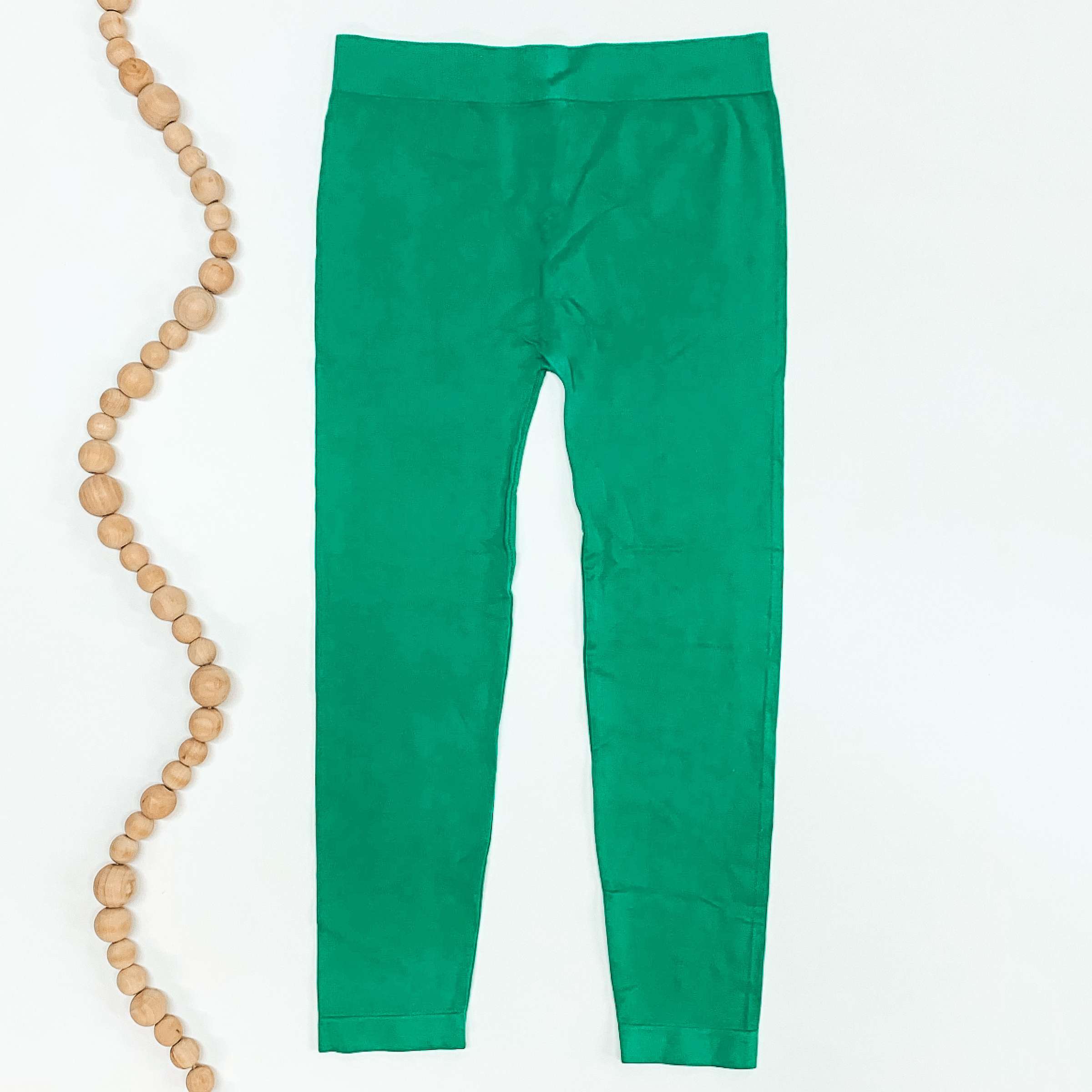 Kelly green colored leggings pictured on a white background with tan beads to the left of the leggings.