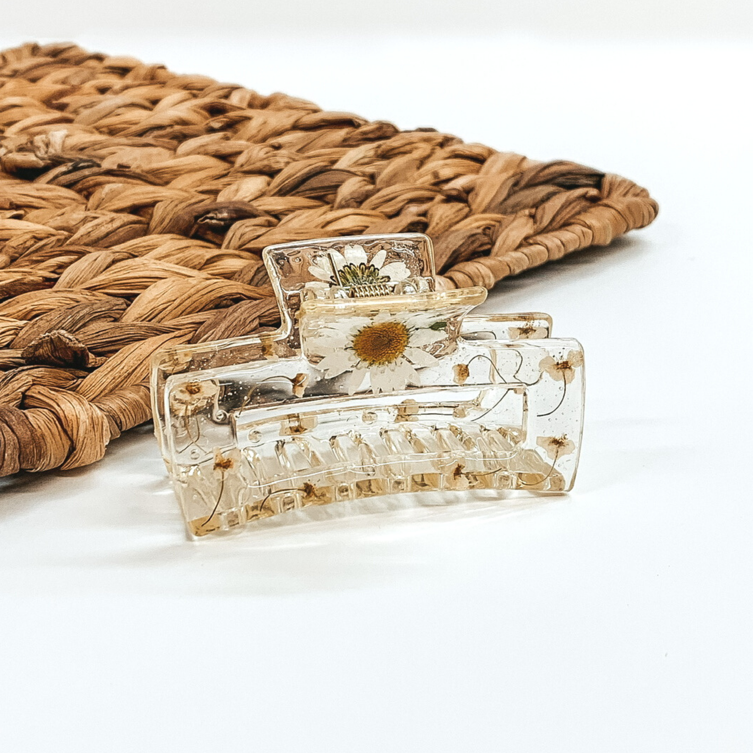 Clear rectangle clip, that has white pressed flowers inside the clip. This clip is pictured on a white background with basket weave behind it.