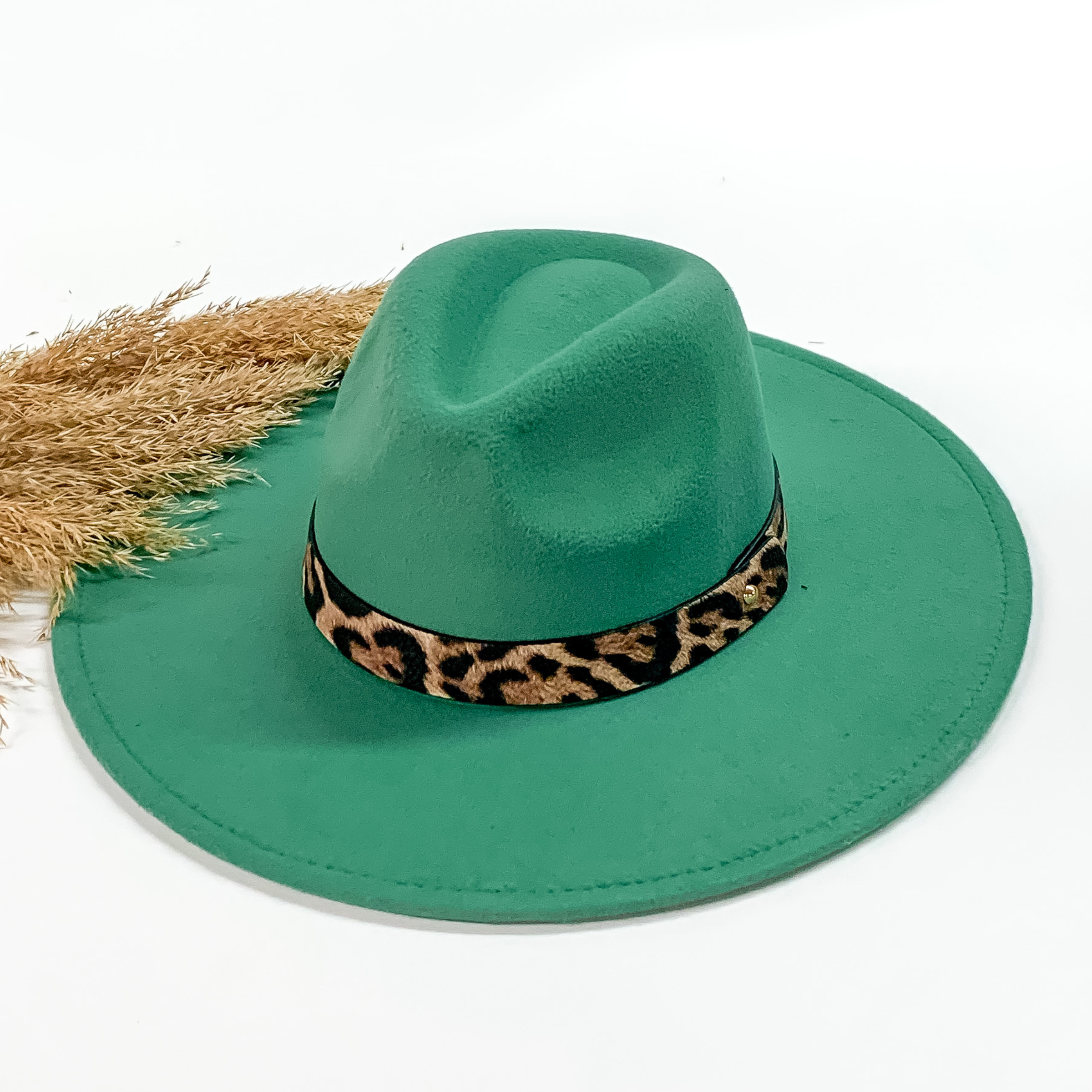 Turquoise faux felt hat with a leopard print hat band. This hat is pictured on a white background with tan pompous in the background.