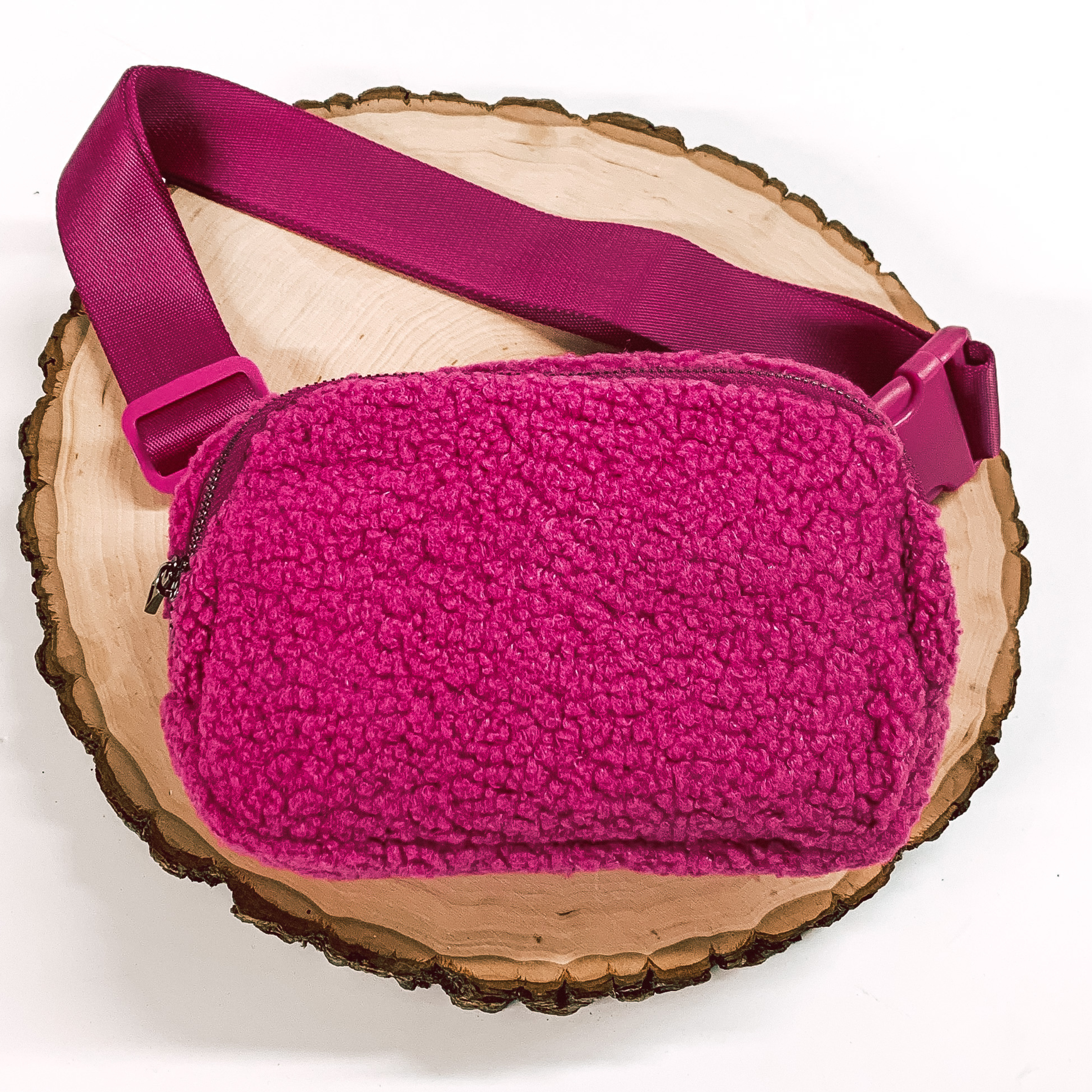 Fuchsia, sherpa fanny pack with a top zipper across the front. This fanny pack also includes fuchsia straps and fuchsia clips. This fanny pack is pictured on a piece of wood on a white background. 