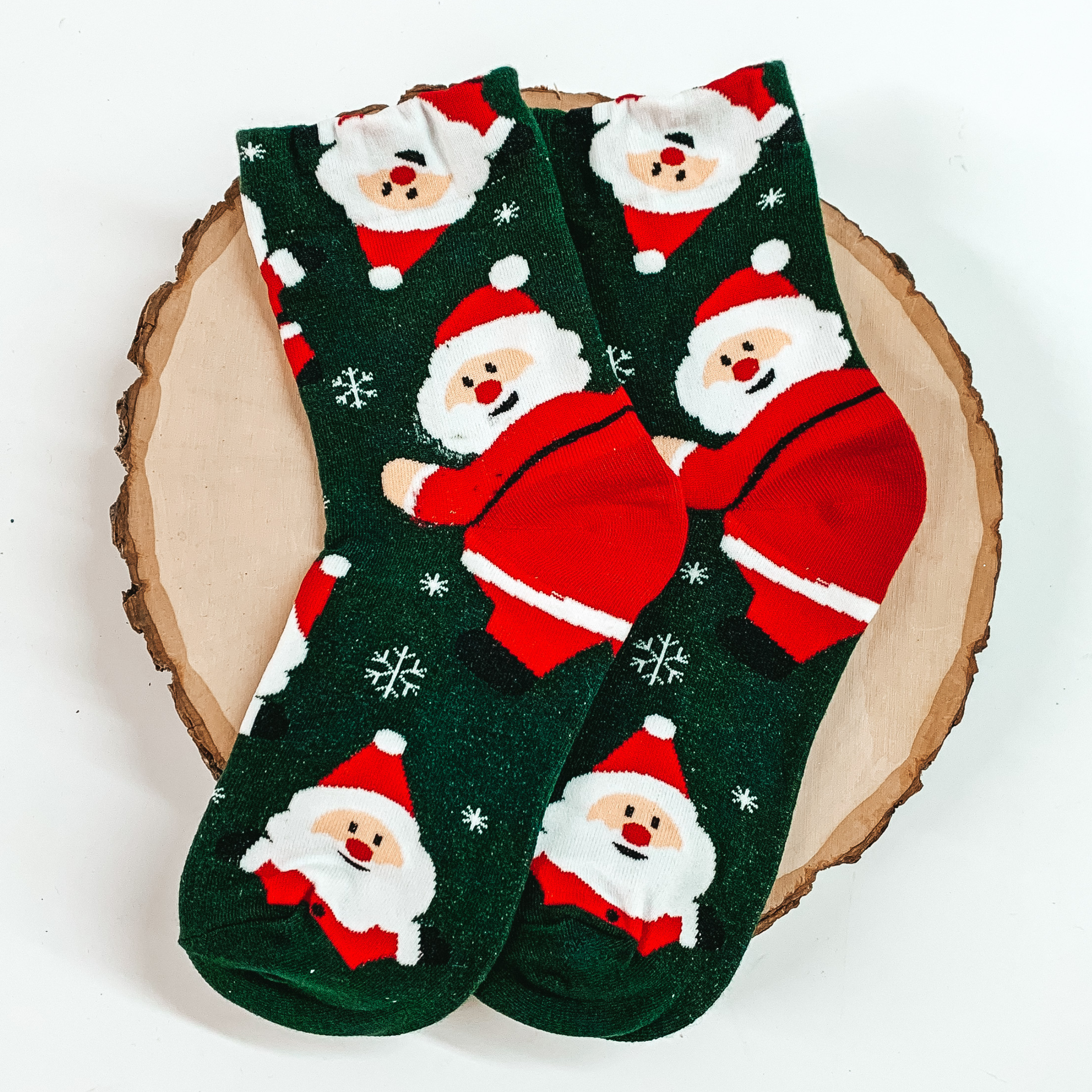 Green ankle socks with a santa claus and snowflake design. These socks are pictured on a piece of wood on a white background. 