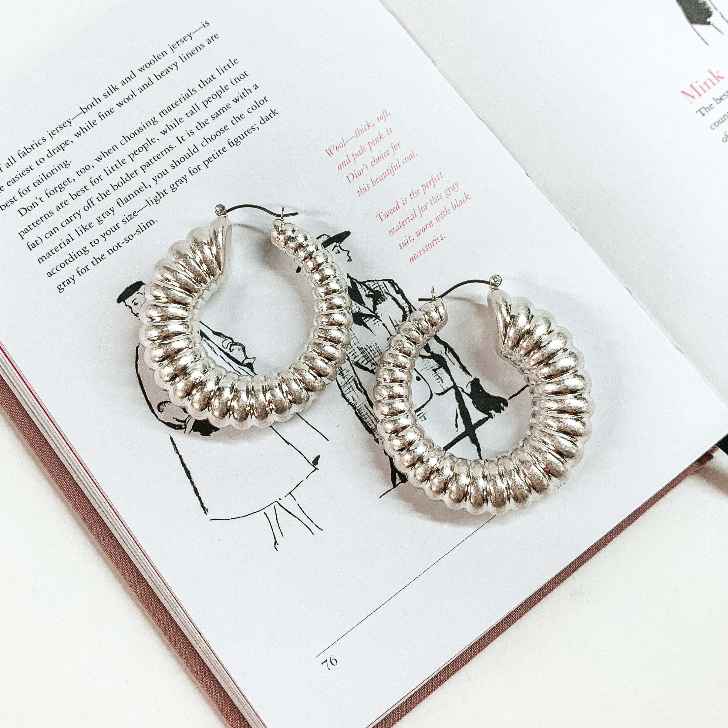 Silver hoop earrings pictured on top of an open book on a white background. 