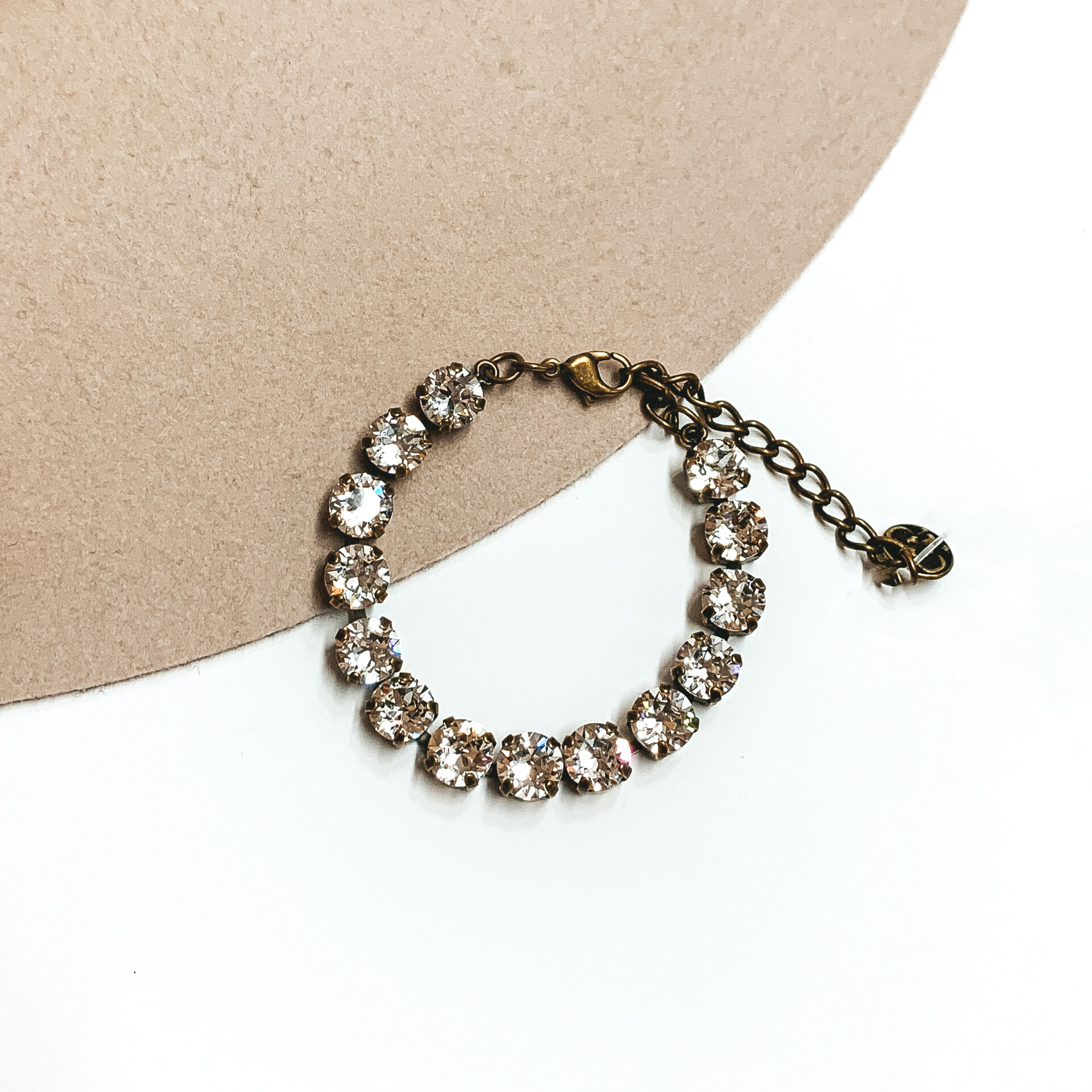 Circle, clear crystal bracelet with a bronze backing. This bracelet is pictured on a white and tan background.
