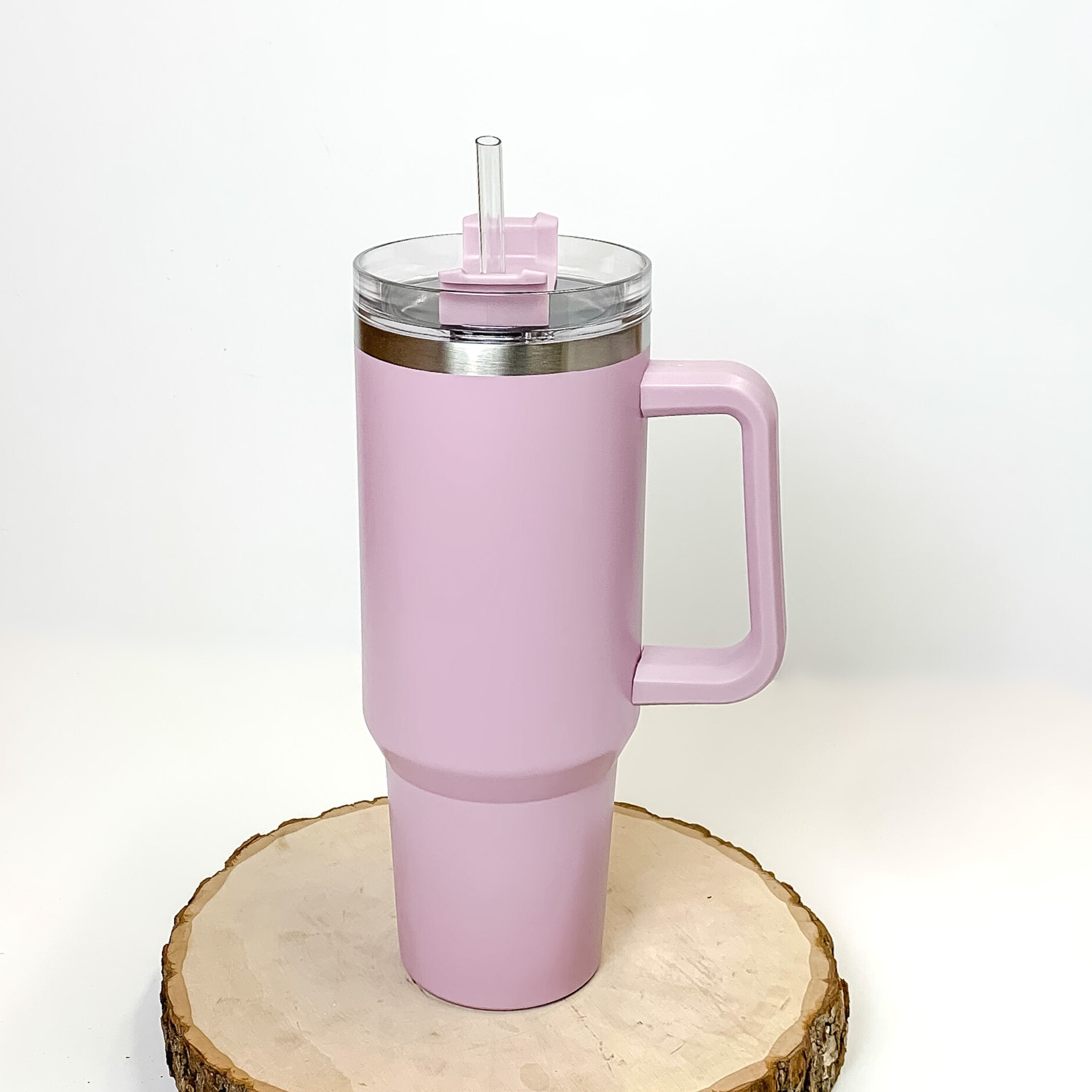 This is a lavender tumbler with a mint handle. This tumbler also has a clear lid and straw. This tumbler is pictured standing on a piece of wood on a white background.