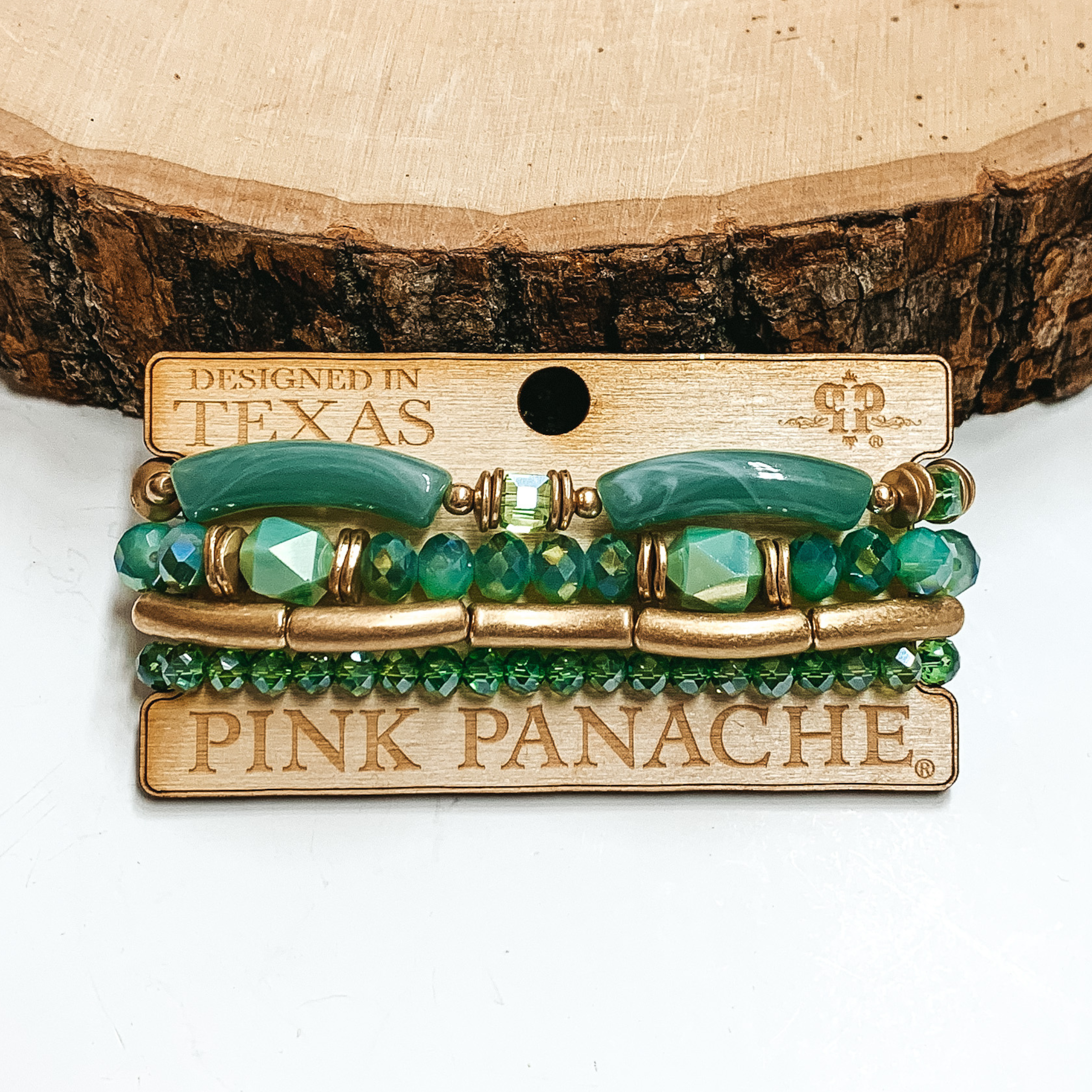 Golg and green bamboo beaded bracelets. There are four bracelets pictured on a wood holder. These bracelets are pictured on front of a wood block on a white background. 