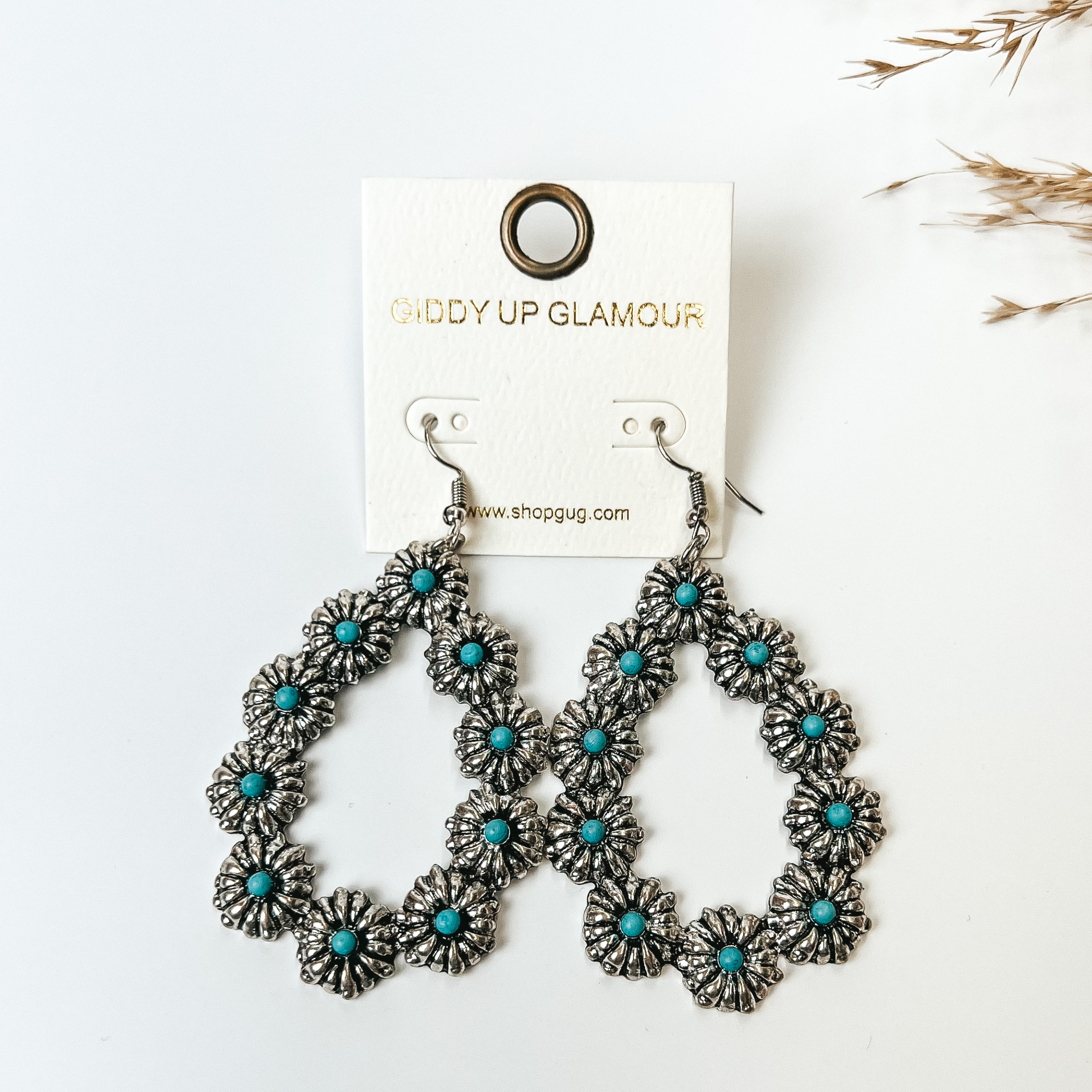 Silver flower concho outline teardrop earrings with center turquoises stones in each concho. These earrings are pictured on a white background. 