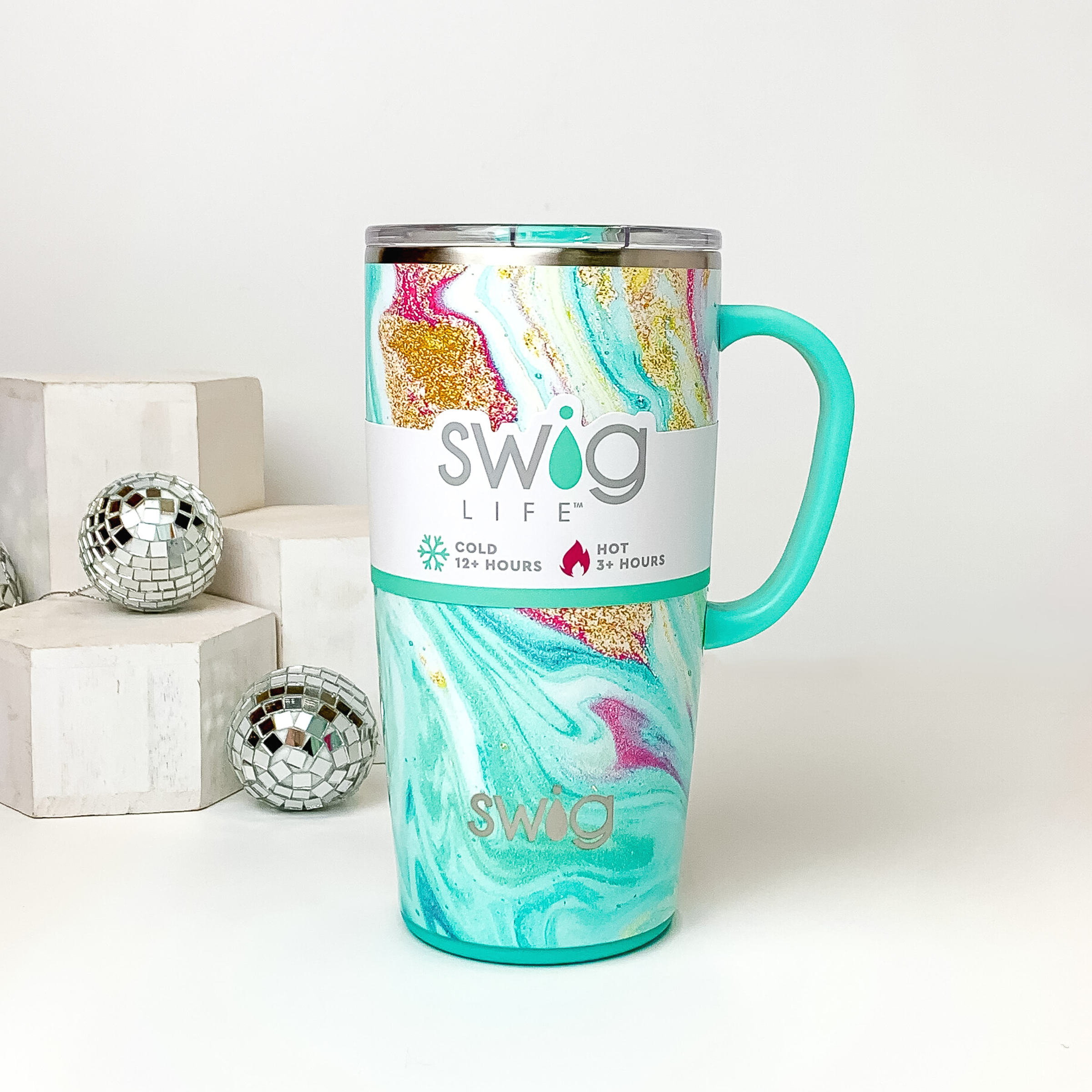Aqua marble mug with a clear lid and aqua handle. This marble print includes shades of blue, pink, and gold glitter. This mug is pictured on a white background with white blocks and disco balls on the left side of the picture. 
