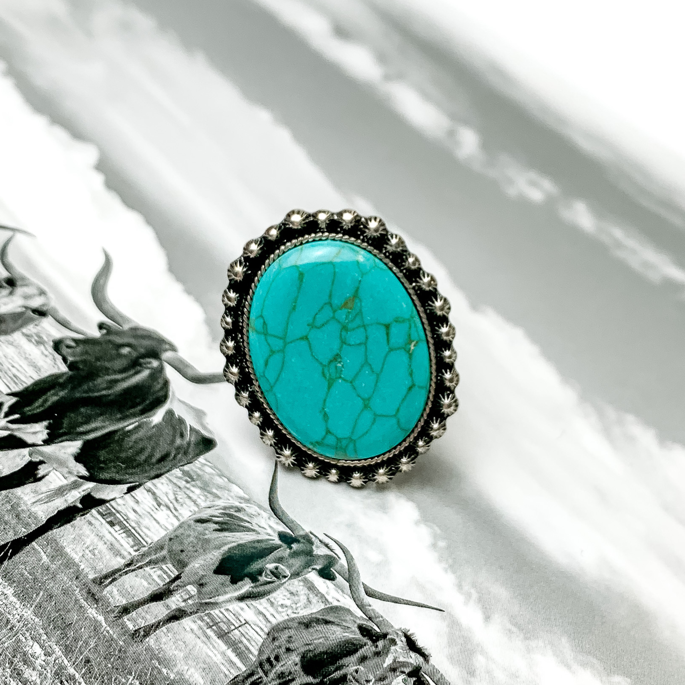 Silver outline ring with a large turquoise center stone. This ring is pictured on a black and white picture. 