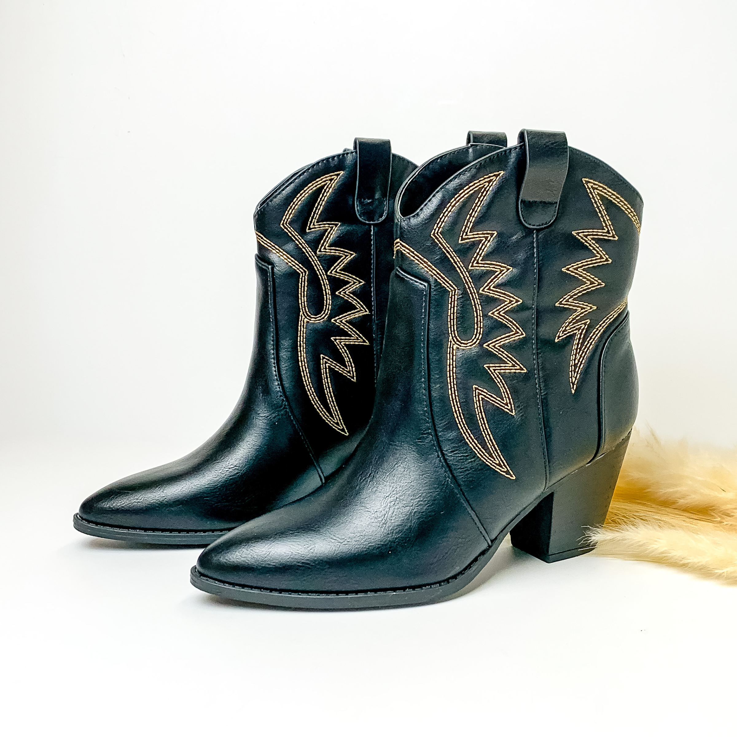 Black ankle booties with ivory western stitching and black heel. These boots are pictured on a white background with some ivory pompous grass on the right side of the boots. 
