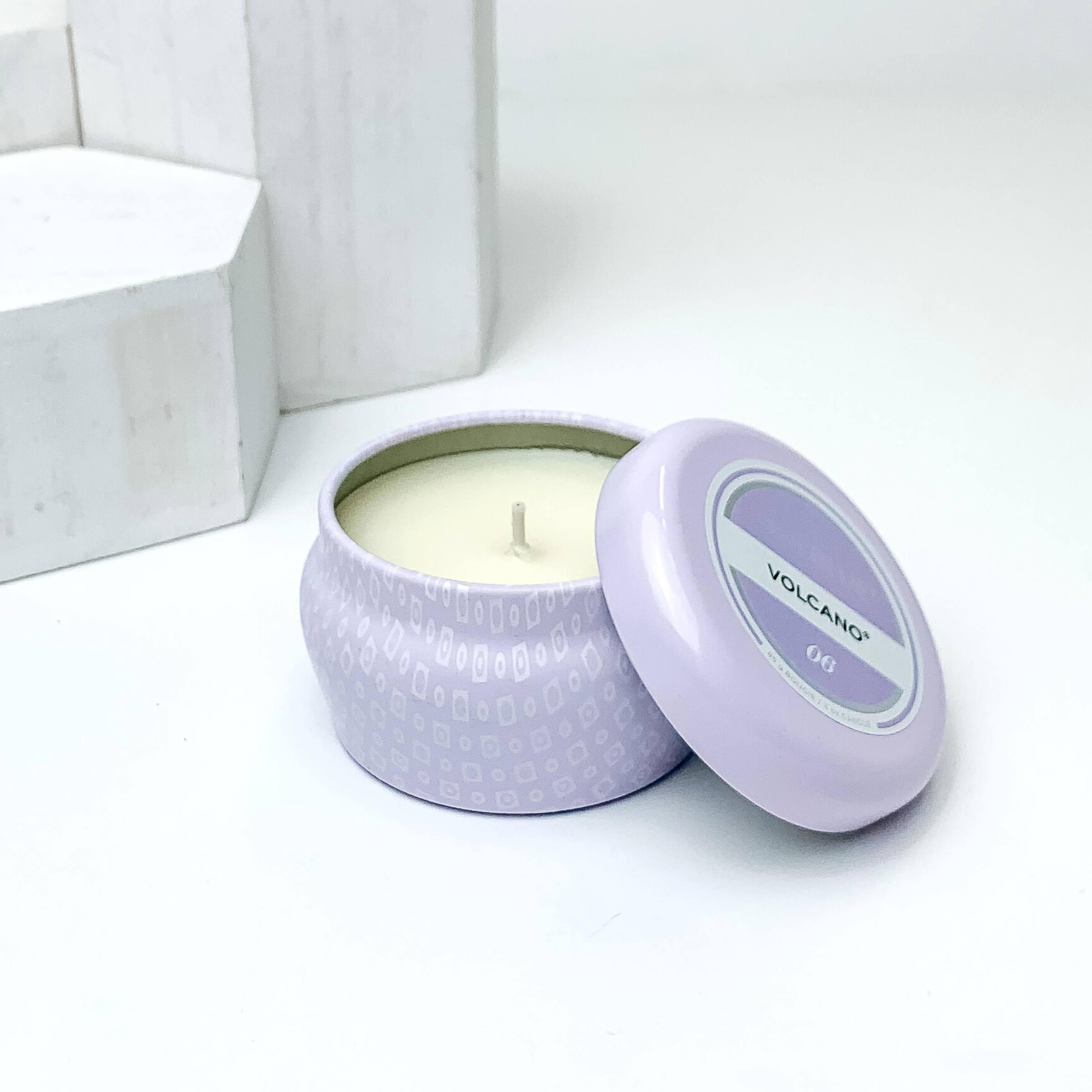 Lavender tin candle with the lid laying against the side. This candle is pictured on a white background. 