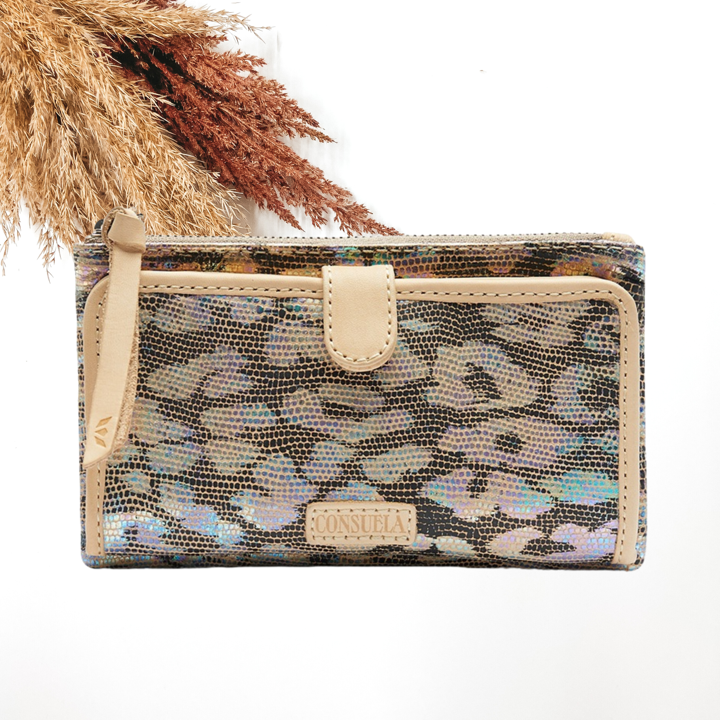 Pictured is a rectangle wallet that has a iridescent, multicolored leopard print design. this wallet includes a front flap with a light tan outline and a top zipper with a light tan zipper pull. This wallet is pictured on a white background with pompous grass in the top left corner. 