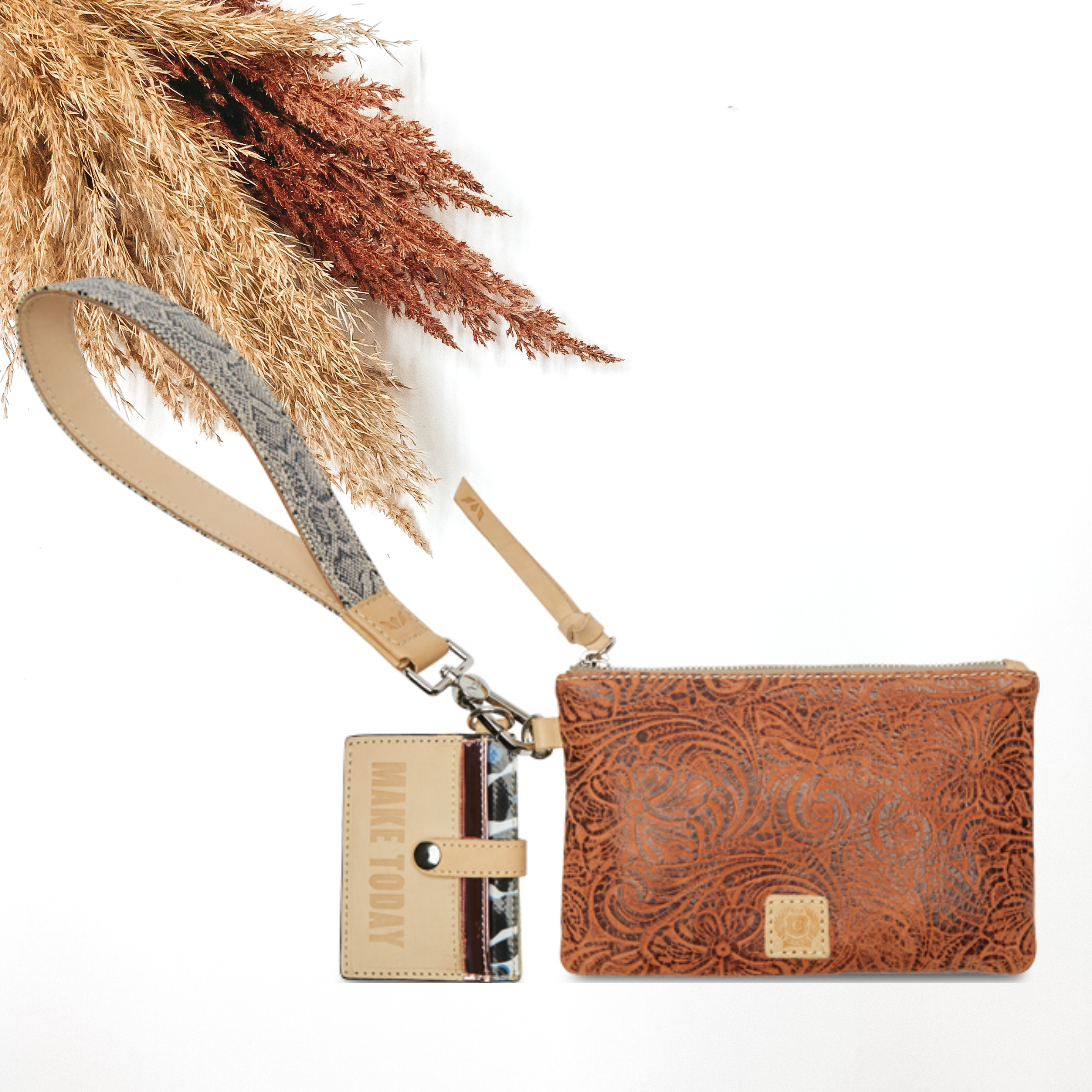 Brown leather tooled pouch with a snakeprint wristelt. This pouch also includes a card holder charm. This is pictured on a white background with tan and brown pompous grass in the background.