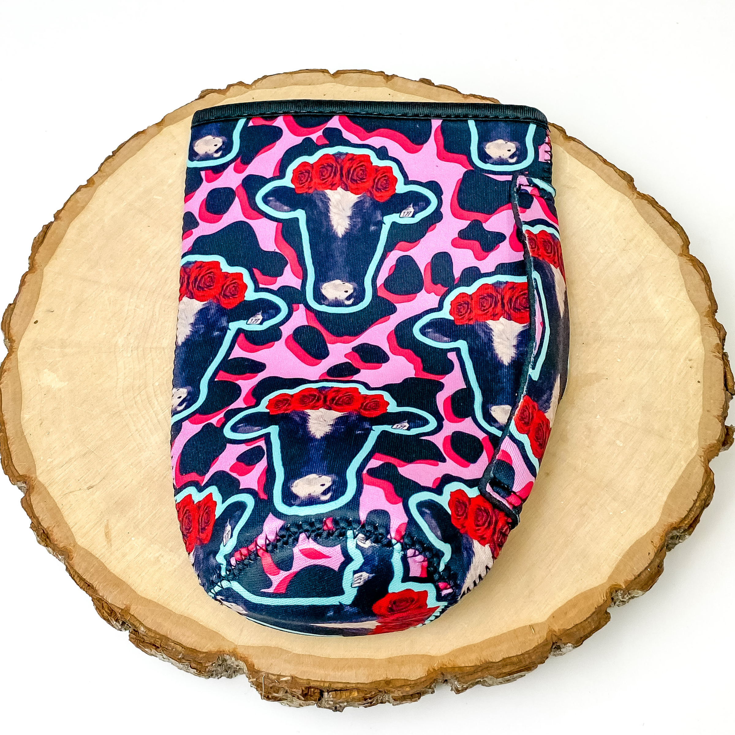 Tumbler drink sleeve with and pink, hot pink, and black cow print design. This drink sleeve also includes a handle and cow head print all over. This drink sleeve is pictured on a piece of wood on a white background. 