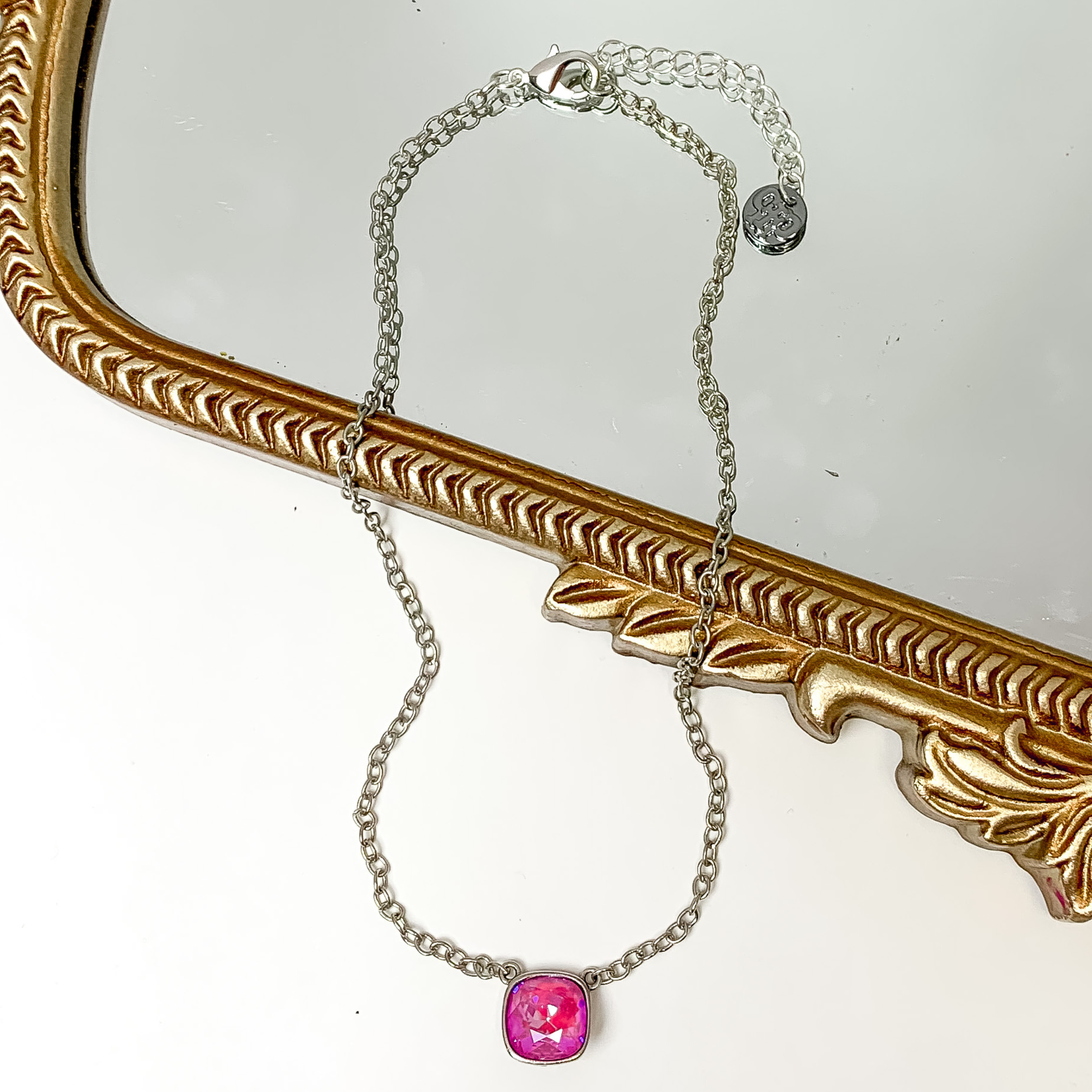 Silver chain necklace with a pink lotus delight cushion cut crystal. This necklace is pictured partially laying on a gold mirror on a white background.