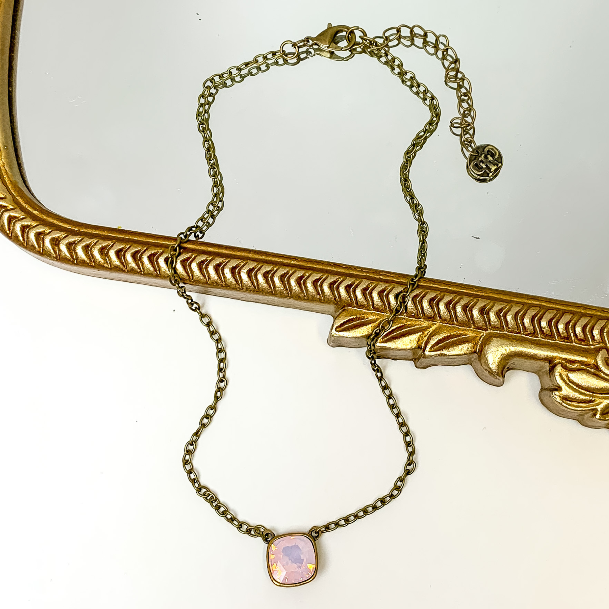 Bronze chain necklace with a rose water opal cushion cut crystal. This necklace is pictured partially laying on a gold mirror on a white background.