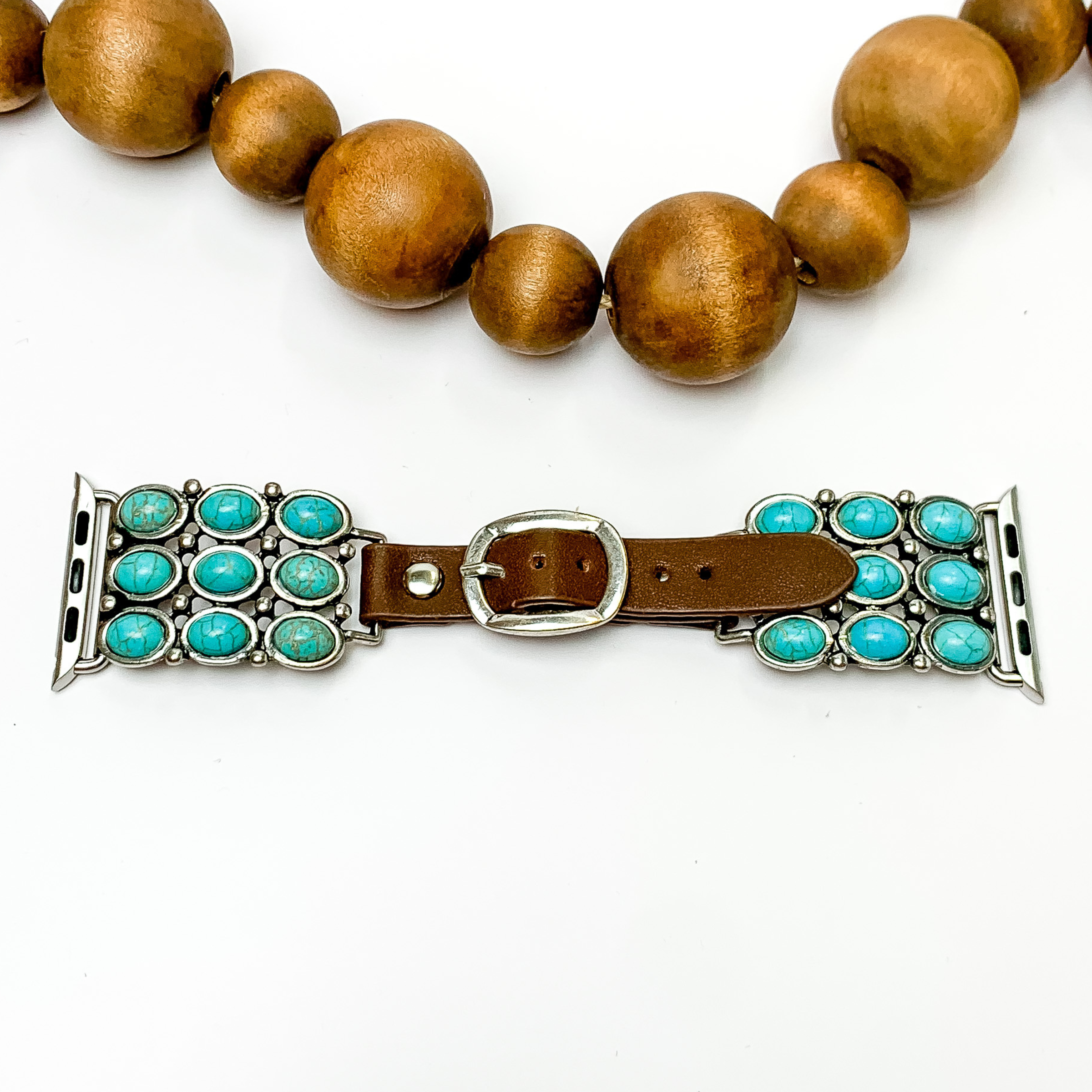 Dark Brown watch band with silver, square ends and nine turquoise stones with Apple watch band acessories. This watch band is pictured on a white background with brown beads underneath the band. 