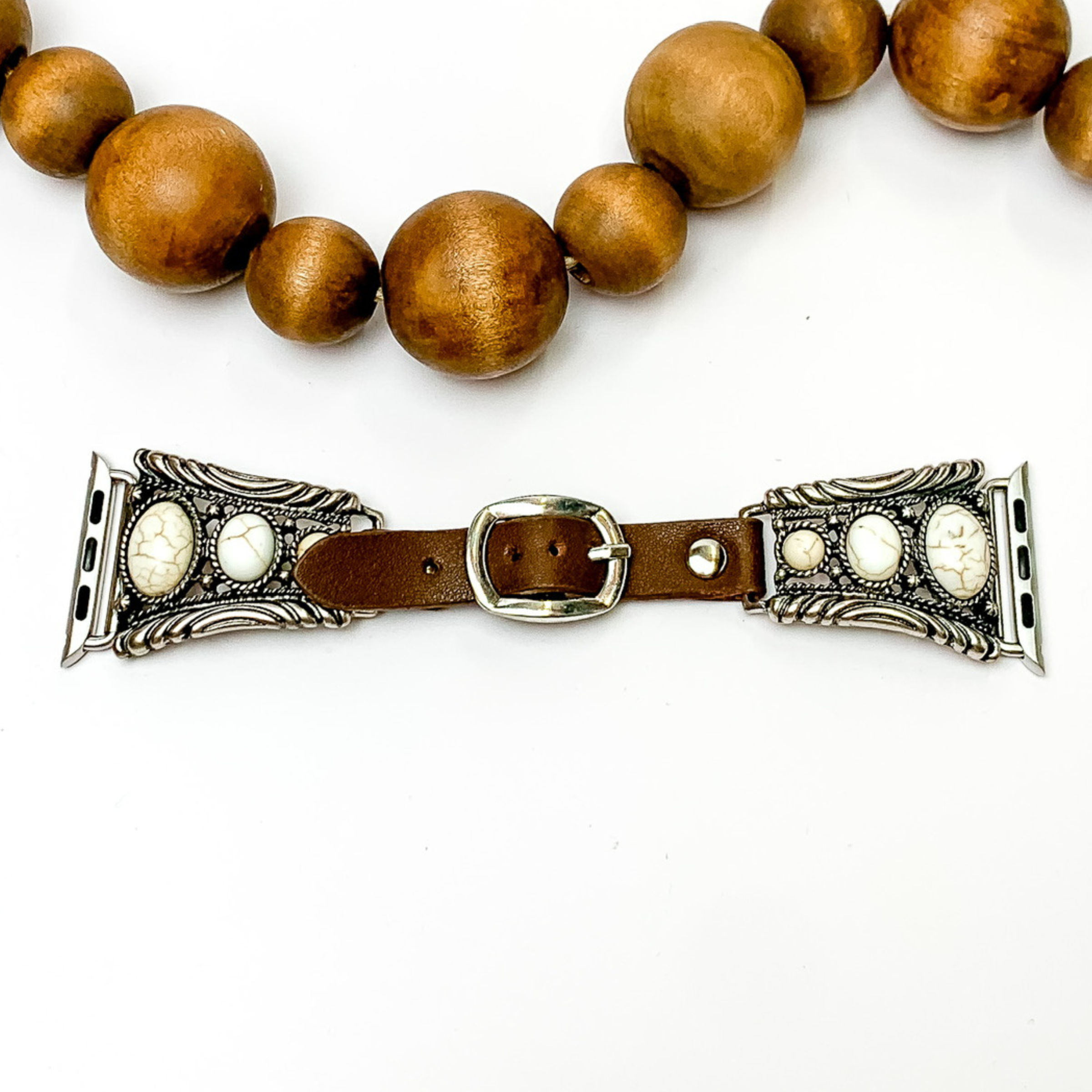Dark Brown watch band with silver, trapesoid shaped ends with Apple watch band acessories. The ends have three ivory stones each going from biggest to smallest. This watch band is pictured on a white background with brown beads above the band. 