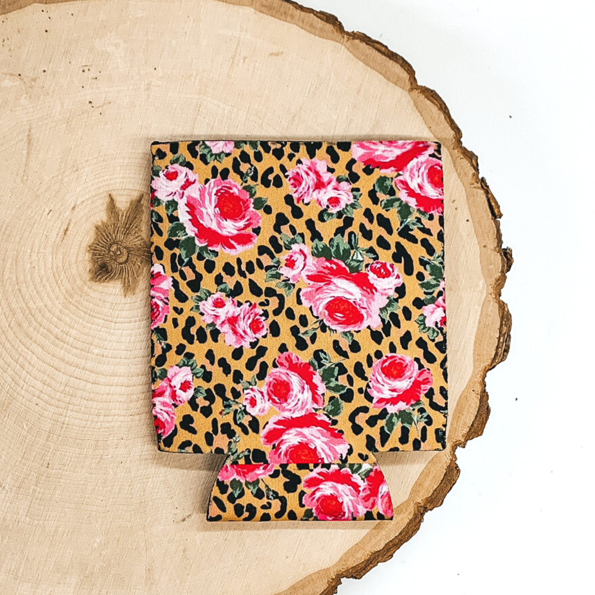 Tan can koozie with black leopard print spots and pink/red roses. This koozie is pictured on a piece of wood on a white background.