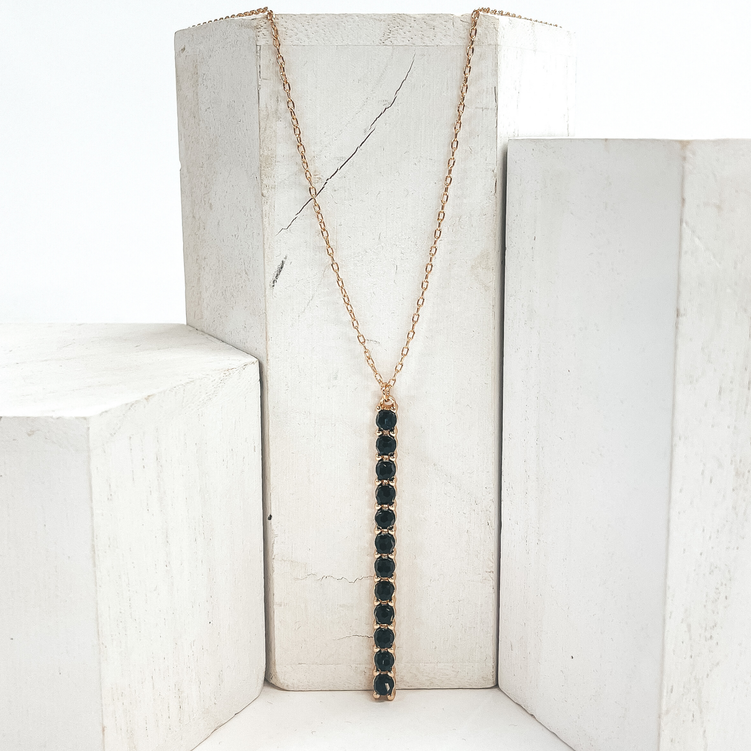 This is a 30 inch adjustable gold necklace with  a gold 2.75 inch bar pendant with black crystal  beads. This necklace is pictured laying on a white  block on a white background with one white block on  each side.