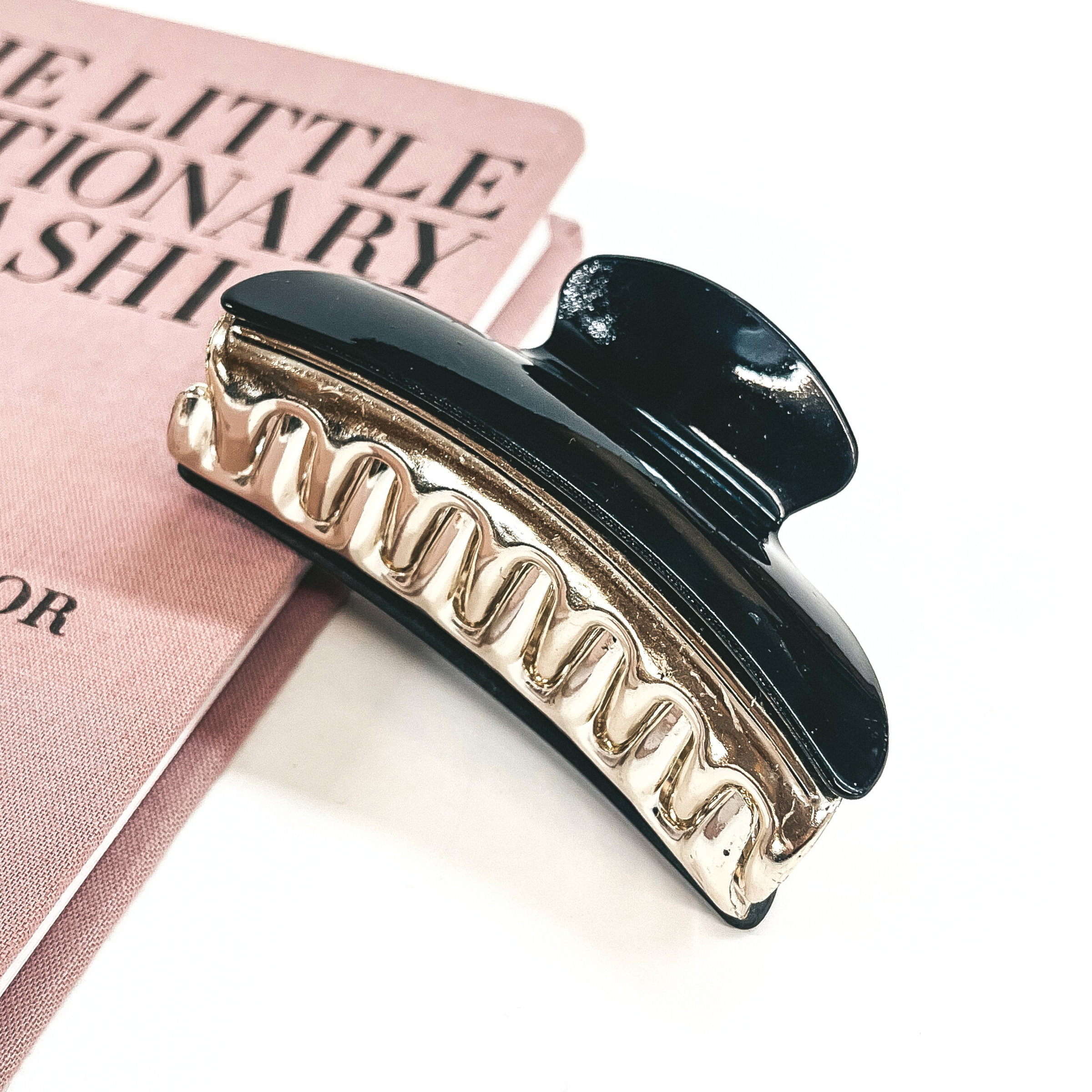 This is a black and gold tone clip leaning on a pink book and white background.