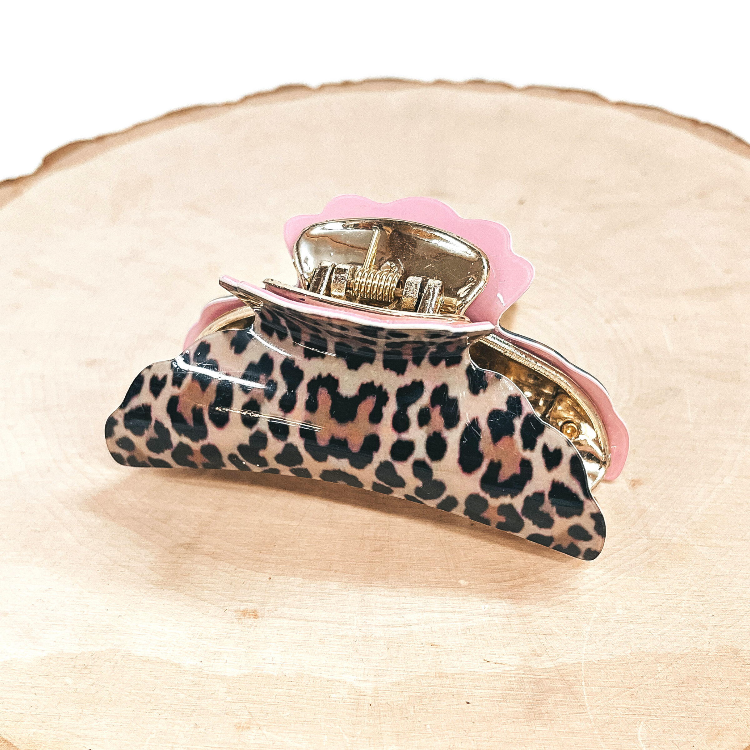 This is a light brown leopard print hair clips in light pink in a gold tone inlay.  This hair clip is  taken on a slab of wood and white background.