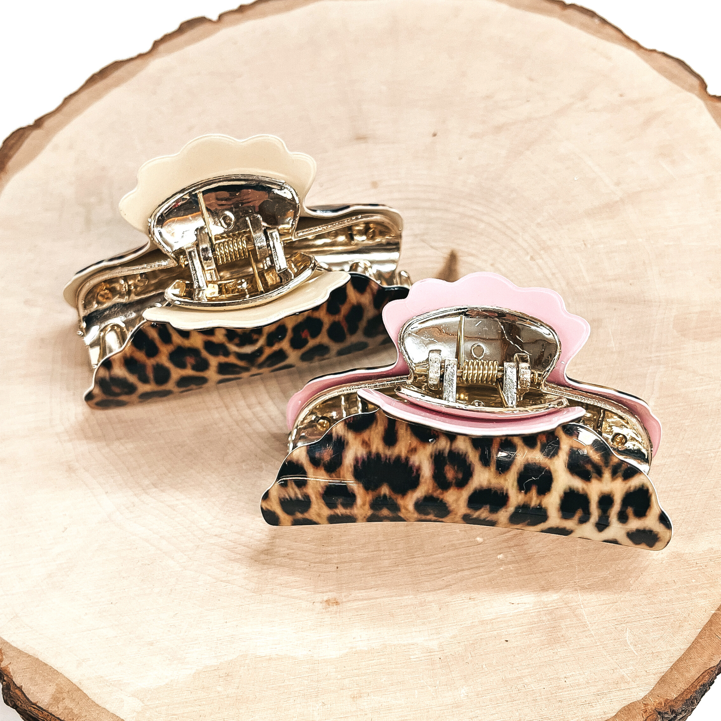 These are yellow leopard print hair clips with a gold tone inlay in light pink and  ivory.   Both of these hair clips are taken on a slab of wood and on a white background.