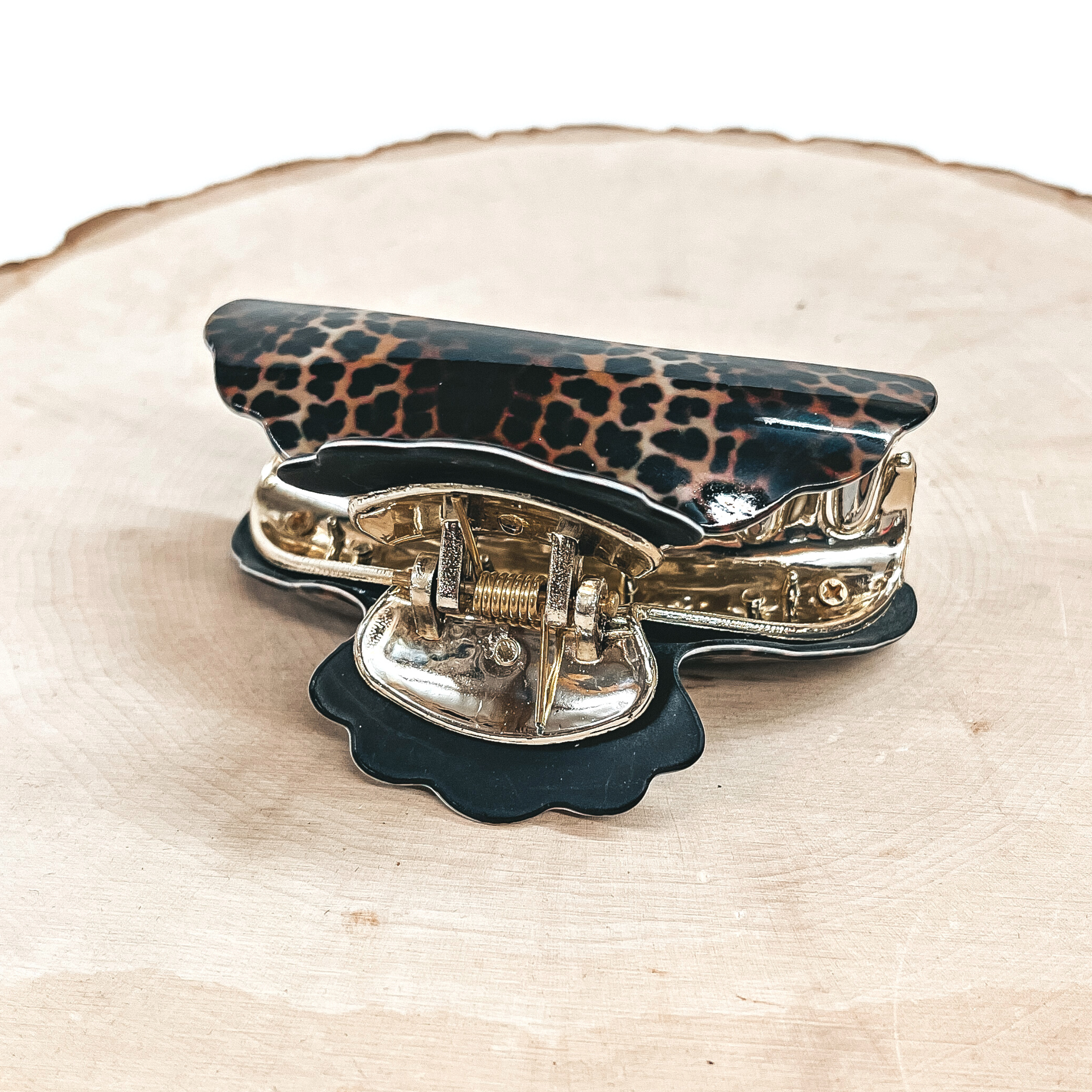 This is a dark leopard print hair clips with a gold tone inlay in black.  This hair clip is taken on a slab of wood and on a white background.