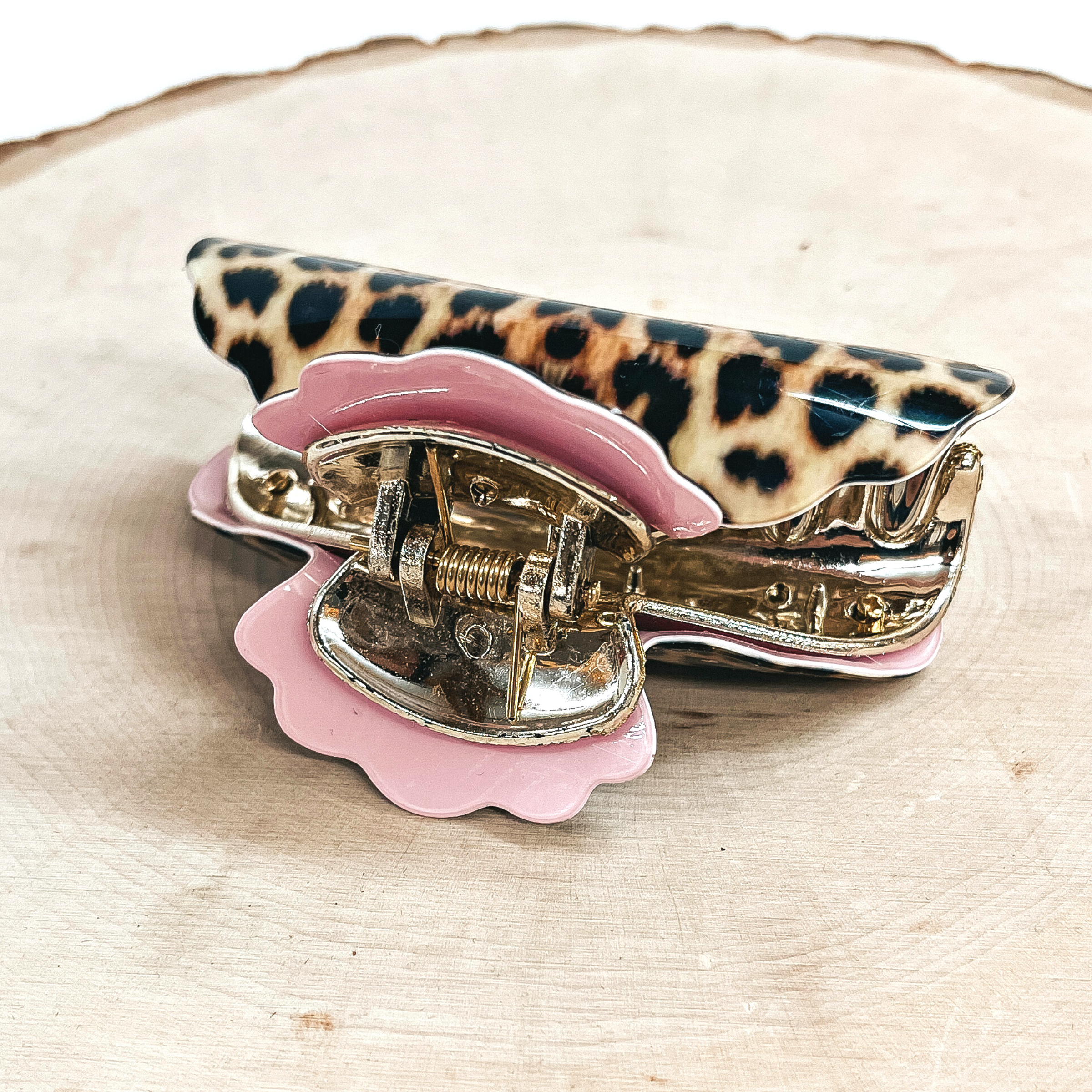 This is a yellow leopard print hair clip with a gold tone inlay in light pink.   This hair clip is taken on a slab of wood and on a white background.