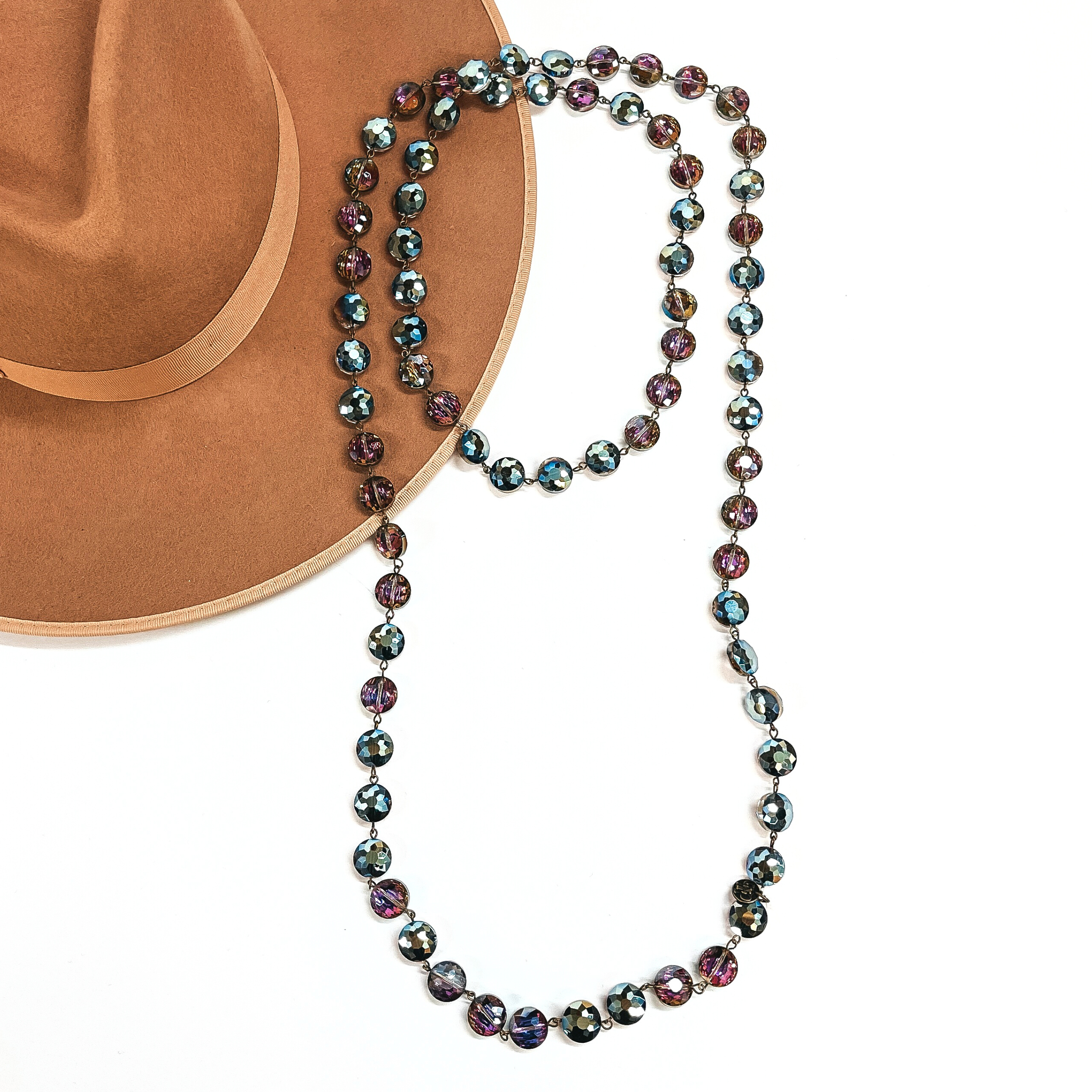This is a long beaded necklace with bronze links connecting the beads. They have flat  round beads in rainbow. This necklace is taken on a camel brown felt hat and on a  white background.