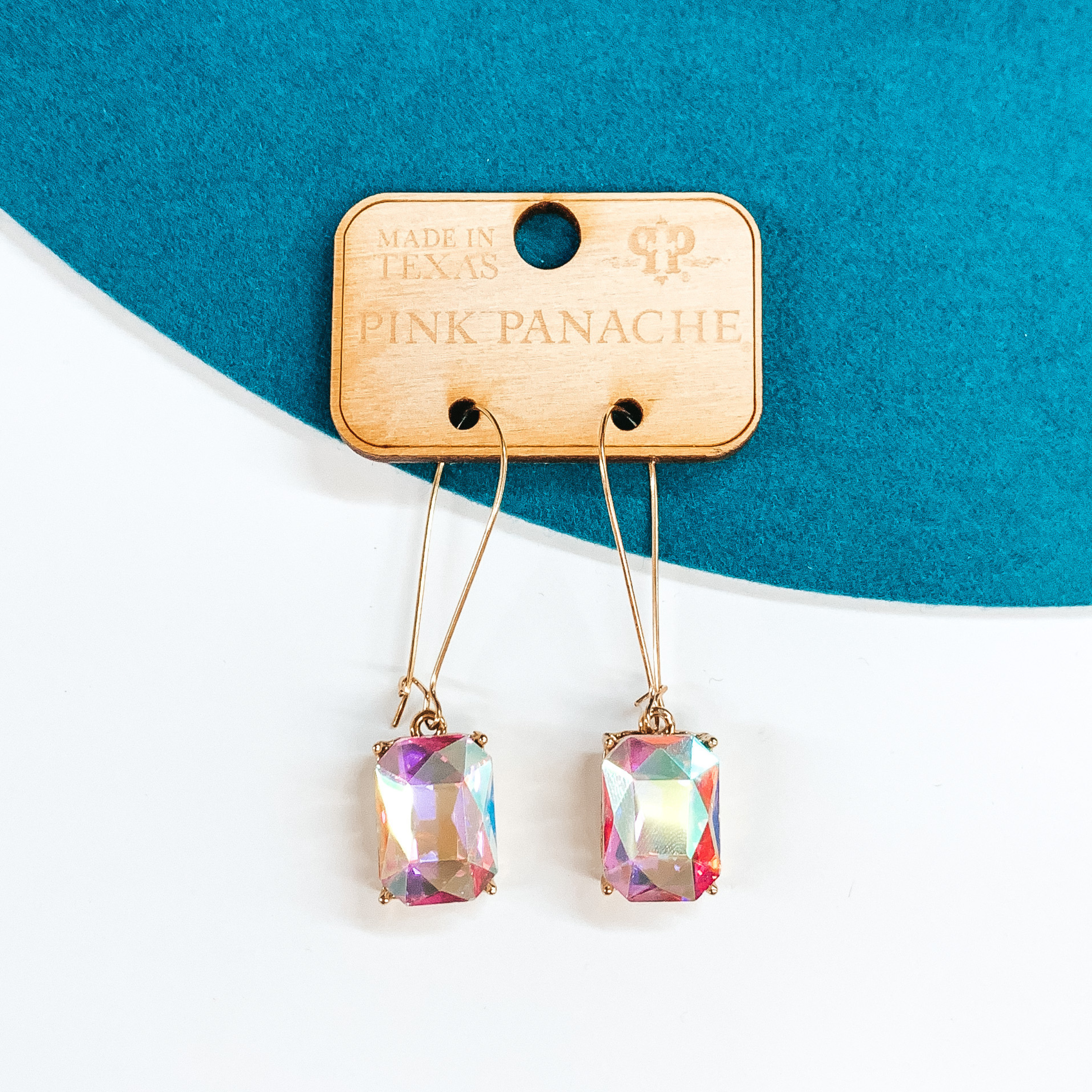 Gold kidney wire earrings with a hanging rectangle AB  crystal pendant. These earrings are pictured on a teal and white background.