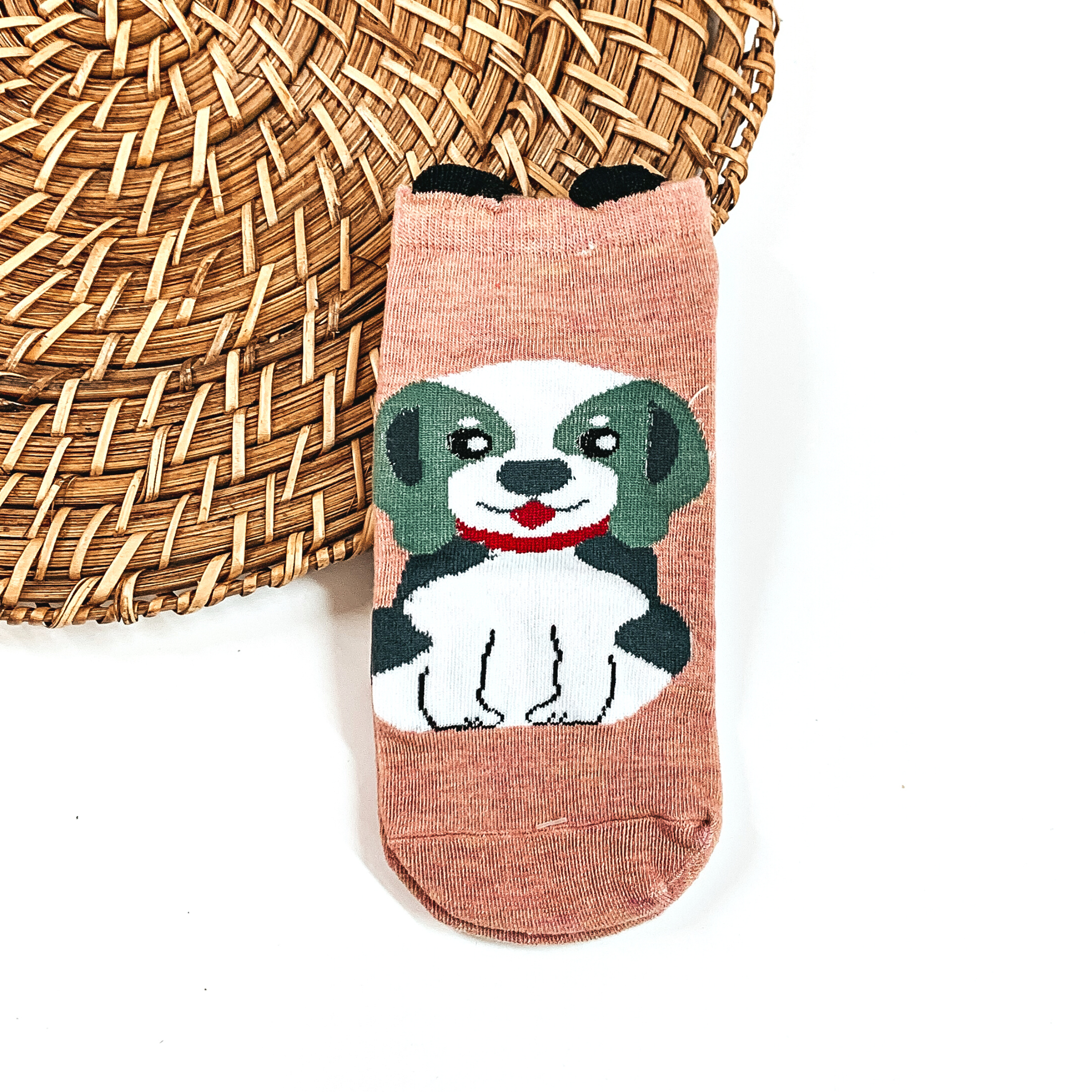 This is a coral pair of socks with a green/white Beagle and red collar. There  are small black ears on top on the socks.  This pair of socks are taken on a brown woven slate and on a white  background.