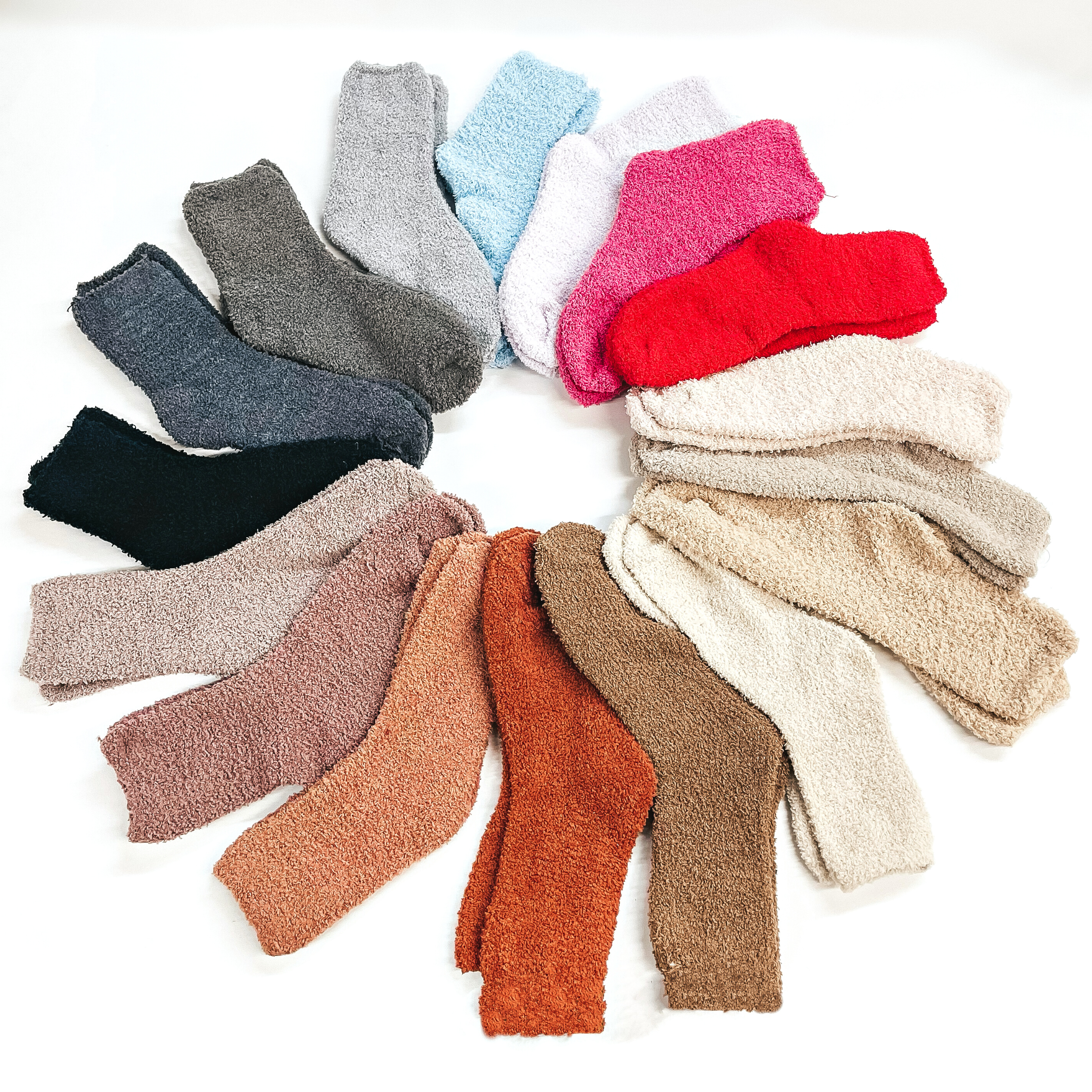 There are seventeen pair of fuzzy socks in assorted colors such as different shades  of grey's, pink/mauve's, nudes/browns, and bright colors such as red, light purple,  and light blue. These pair of socks are taken on a white background and made into a  circle/spiral.