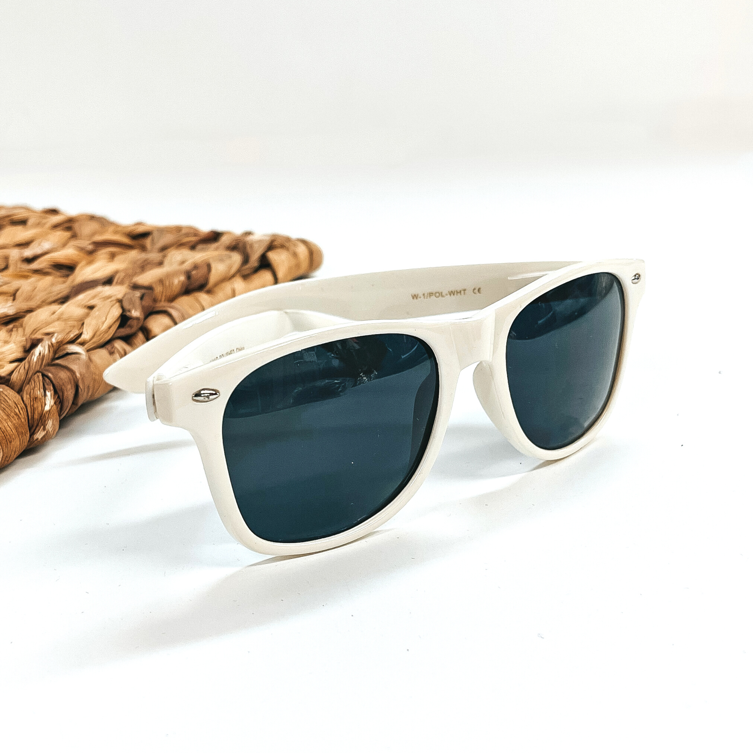 This is a white frame round sunglasses with a black/dark grey lense with small silver  detailing. This pair of sunglasses are taken on a white background with a brown  woven slate in the side as decor.