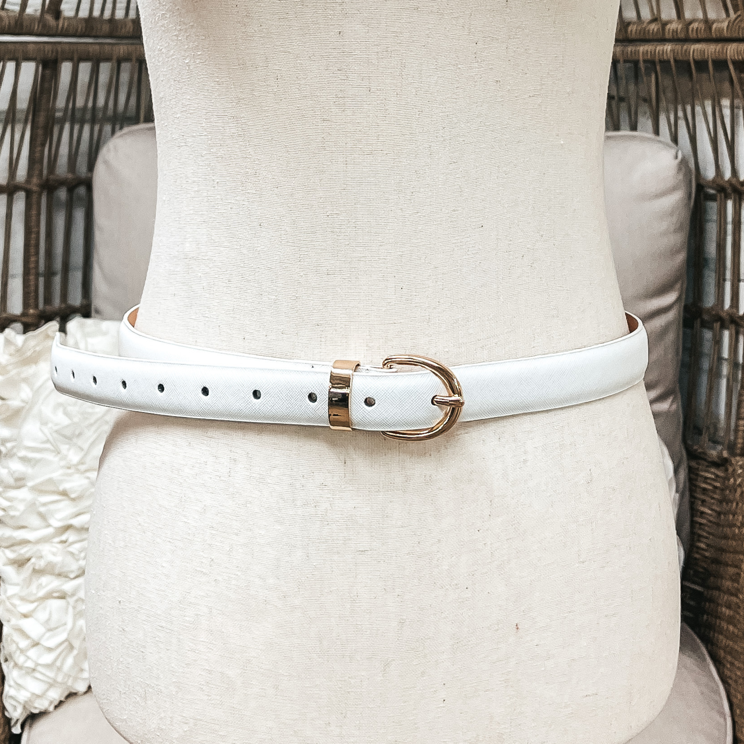There is one skinny belt in white with a small oval buckle in gold. The belt  is placed on an ivory mannequin.