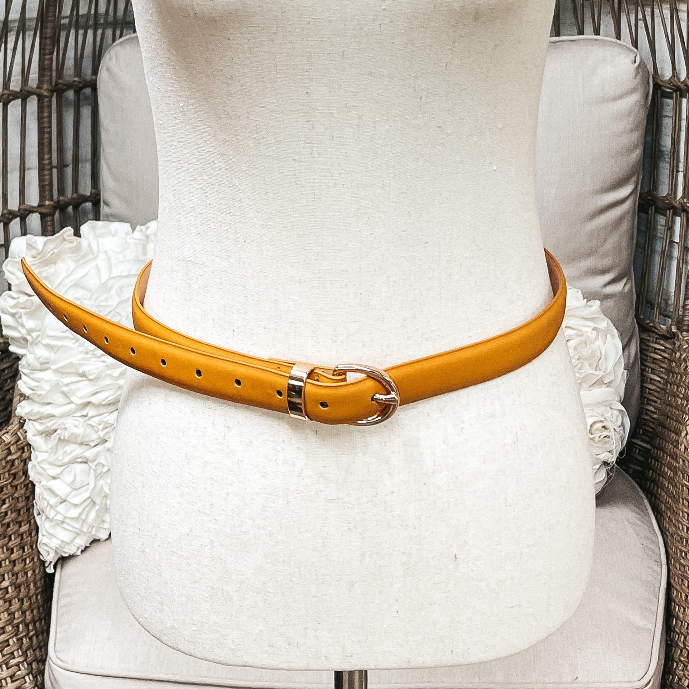 There is one skinny belt in mustard yellow with a small oval buckle in gold. The belt  is placed on an ivory mannequin.