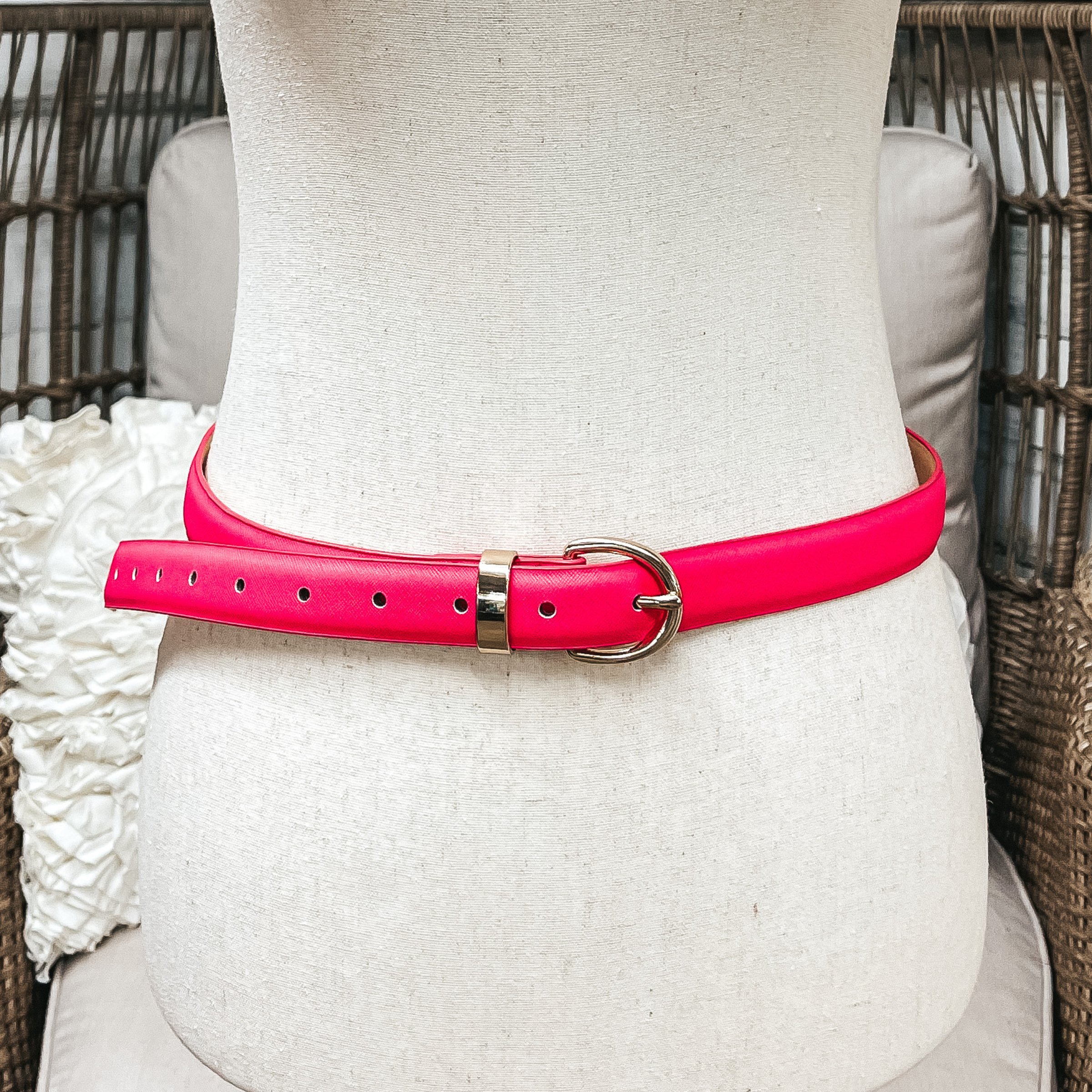 There is one skinny belt in hot pink with a small oval buckle in gold. The belt  is placed on an ivory mannequin.