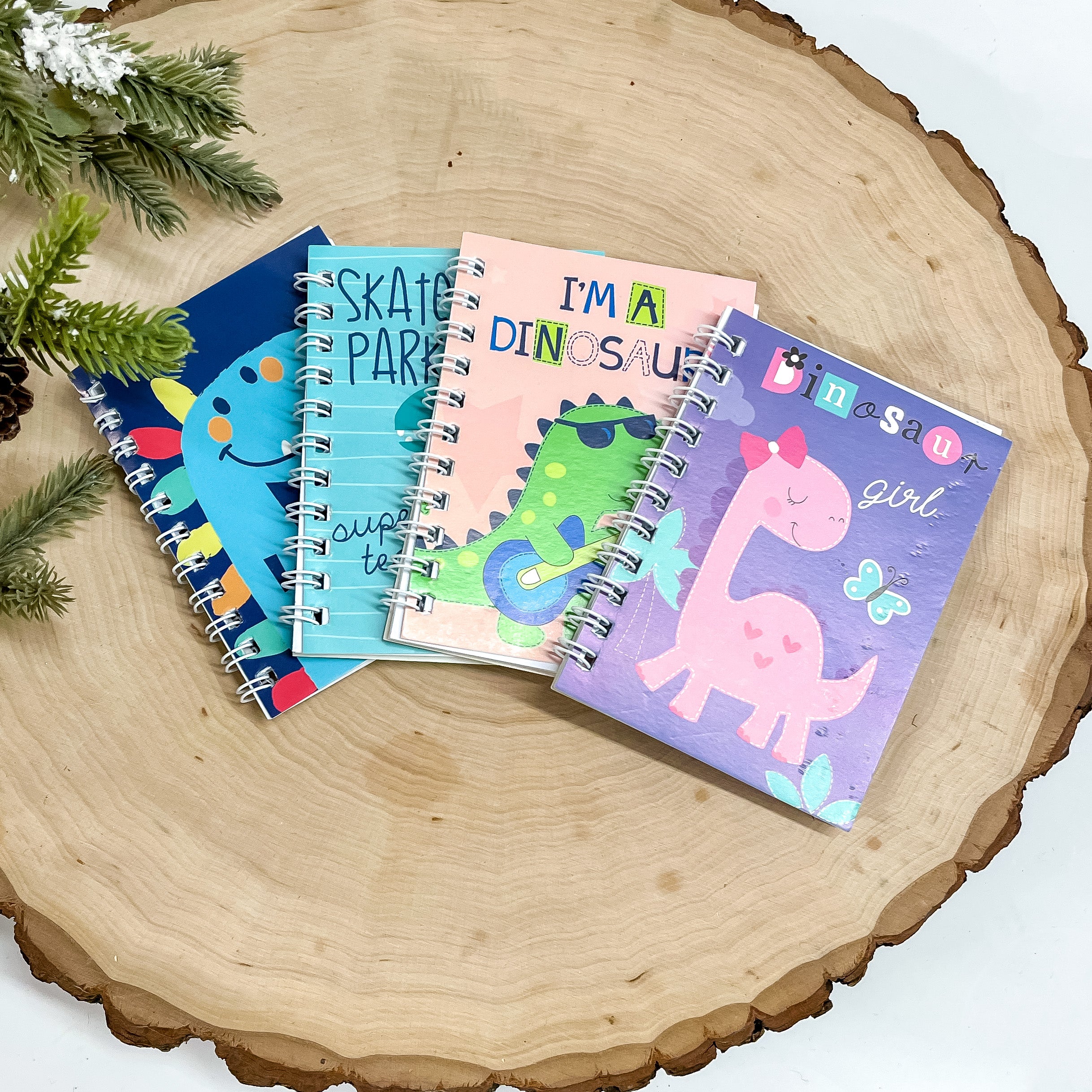 Four small books with dinosaurs on the covers are pictured on a piece of wood. This is all pictured on a white background. 