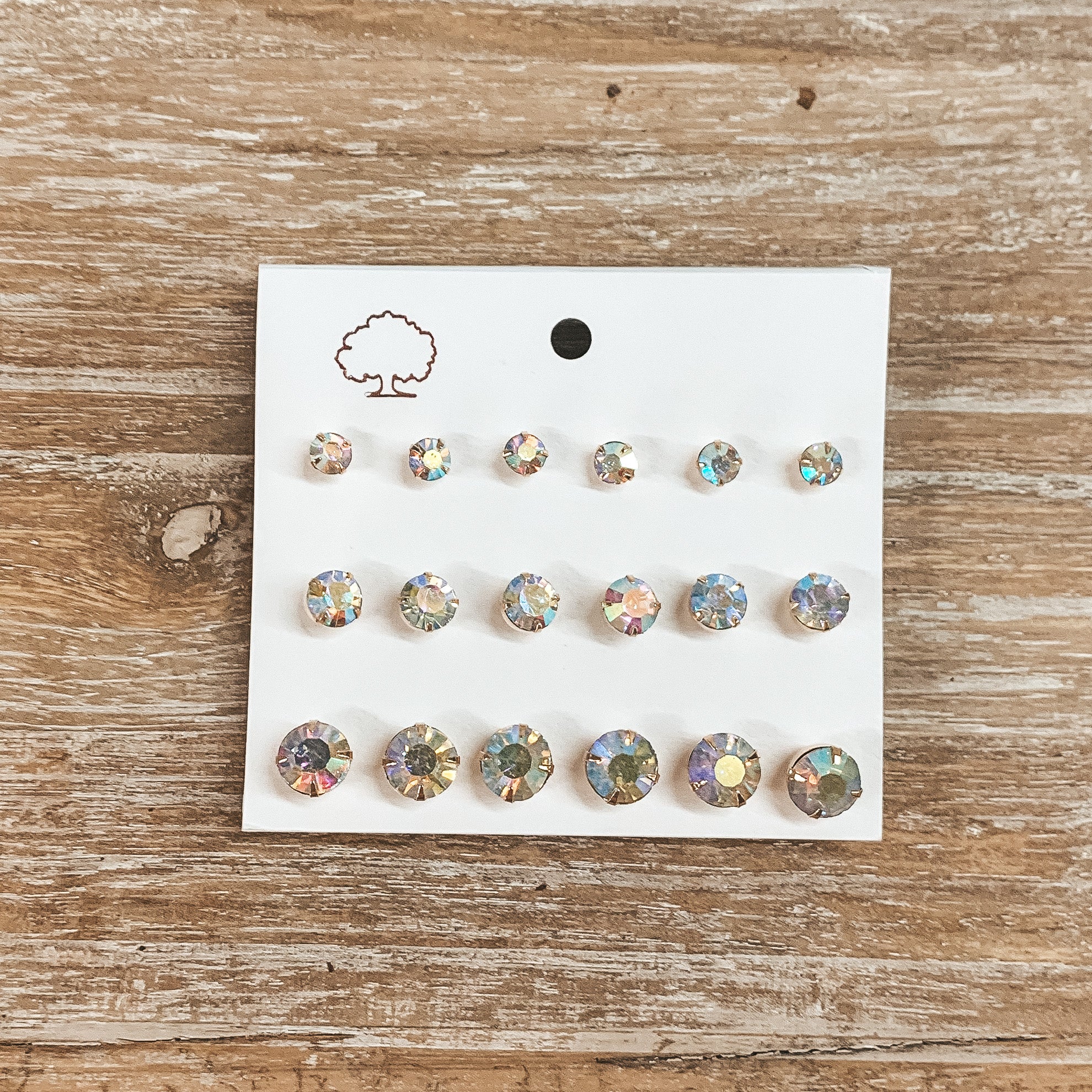 This is a pack of nine ab crystal stud earrings in different sizes. These earrings are on a white earring card holder and taken on a wooden slate.