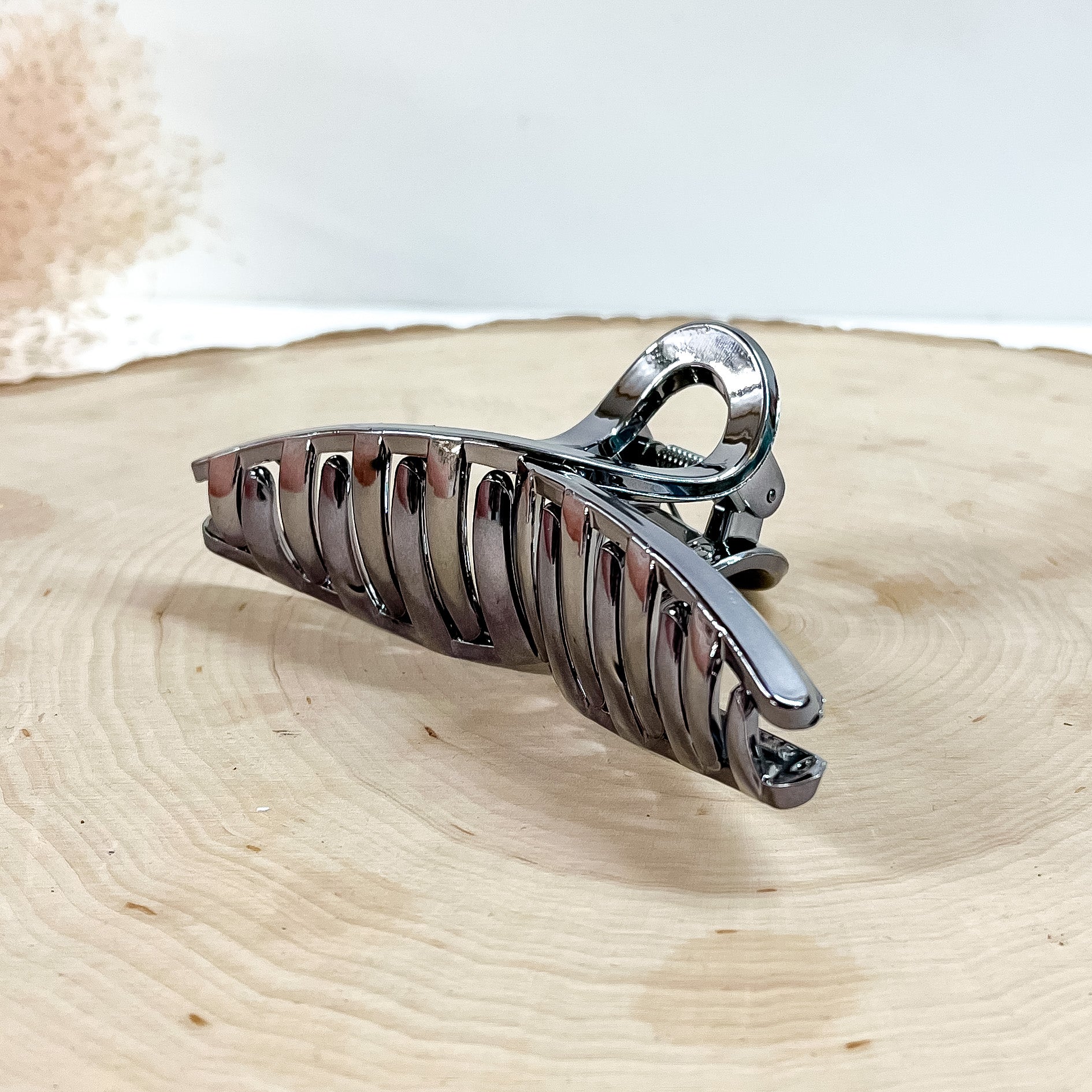 This is a long loop metallic hair clip in gunmetal,  this clip is taken on a  slab of wood and in white background with a plant in the side as decor.
