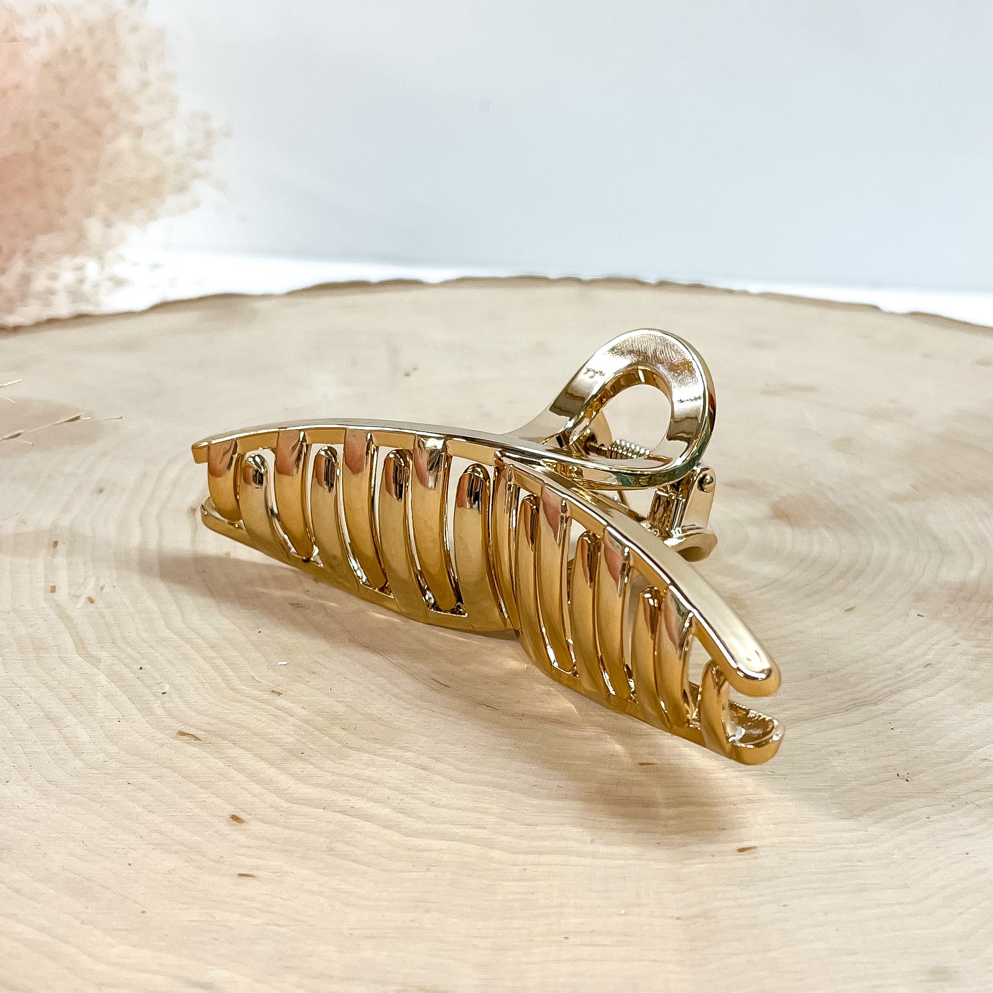 This is a long loop metallic hair clip in cooper/rose gold,  this clip is taken on a  slab of wood and in white background with a plant in the side as decor.
