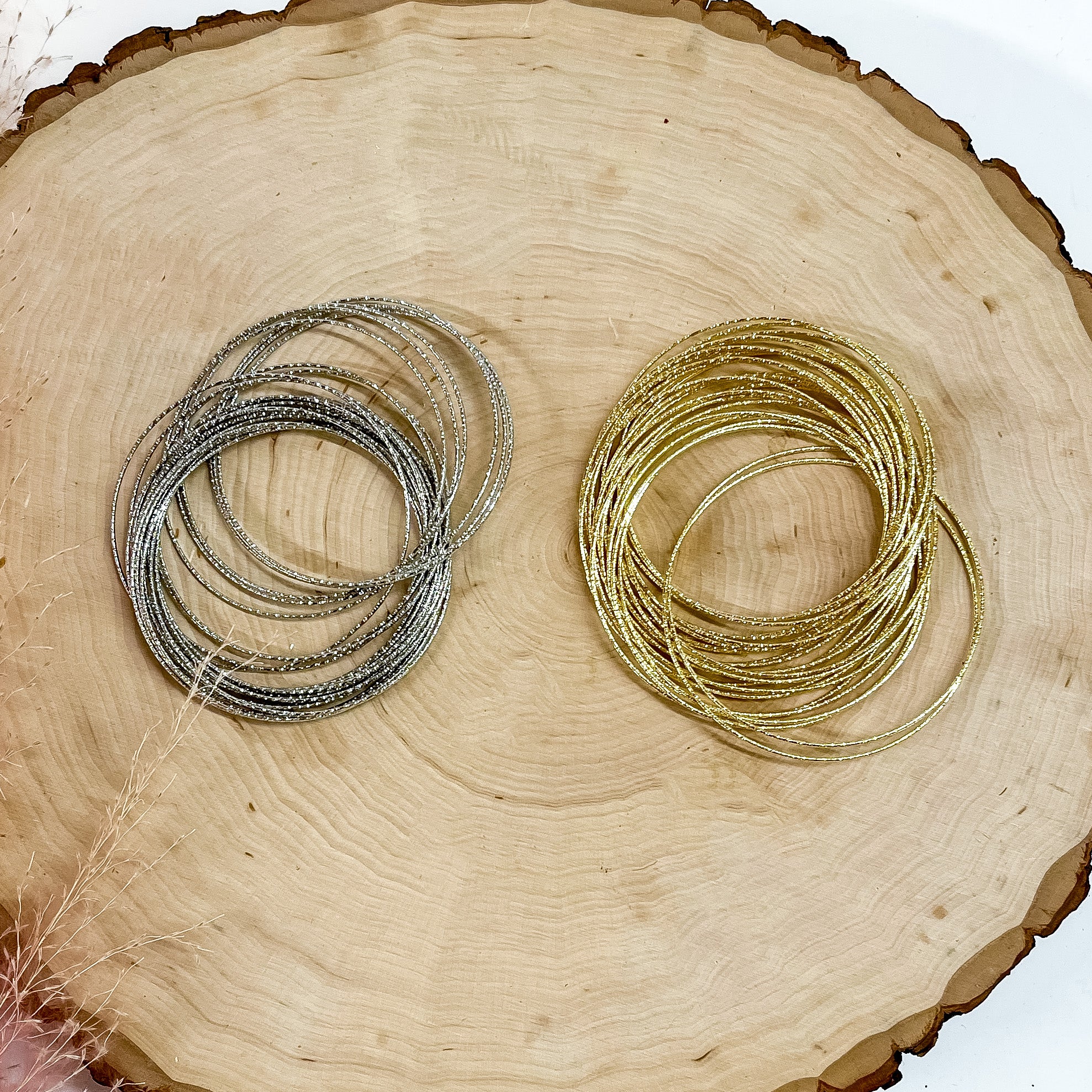 Pictured on a piece of wood are two bracelet bangle sets. One set is in silver and the other set is in gold. 