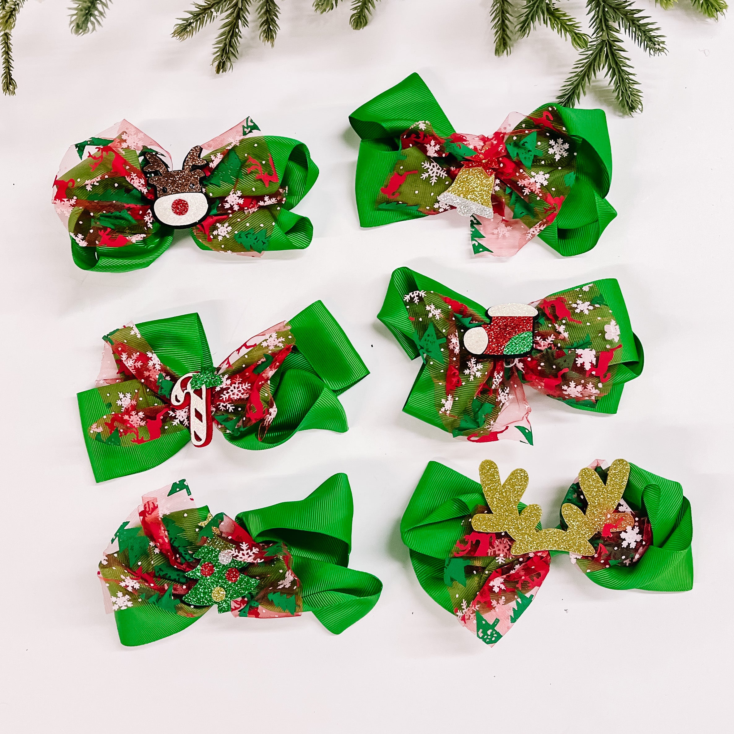 Pictured on a white background are six green bows. Each bow has a unique christmas charm in the center. 